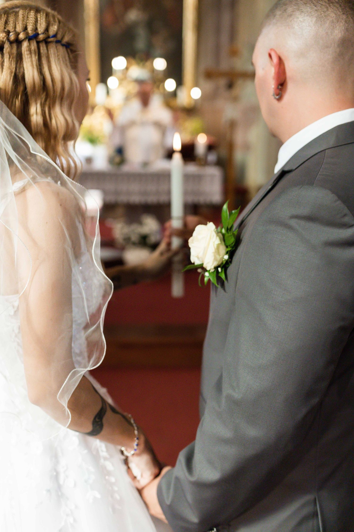 A bride and groom stand together during their wedding ceremony in a church with soft lighting and candles.