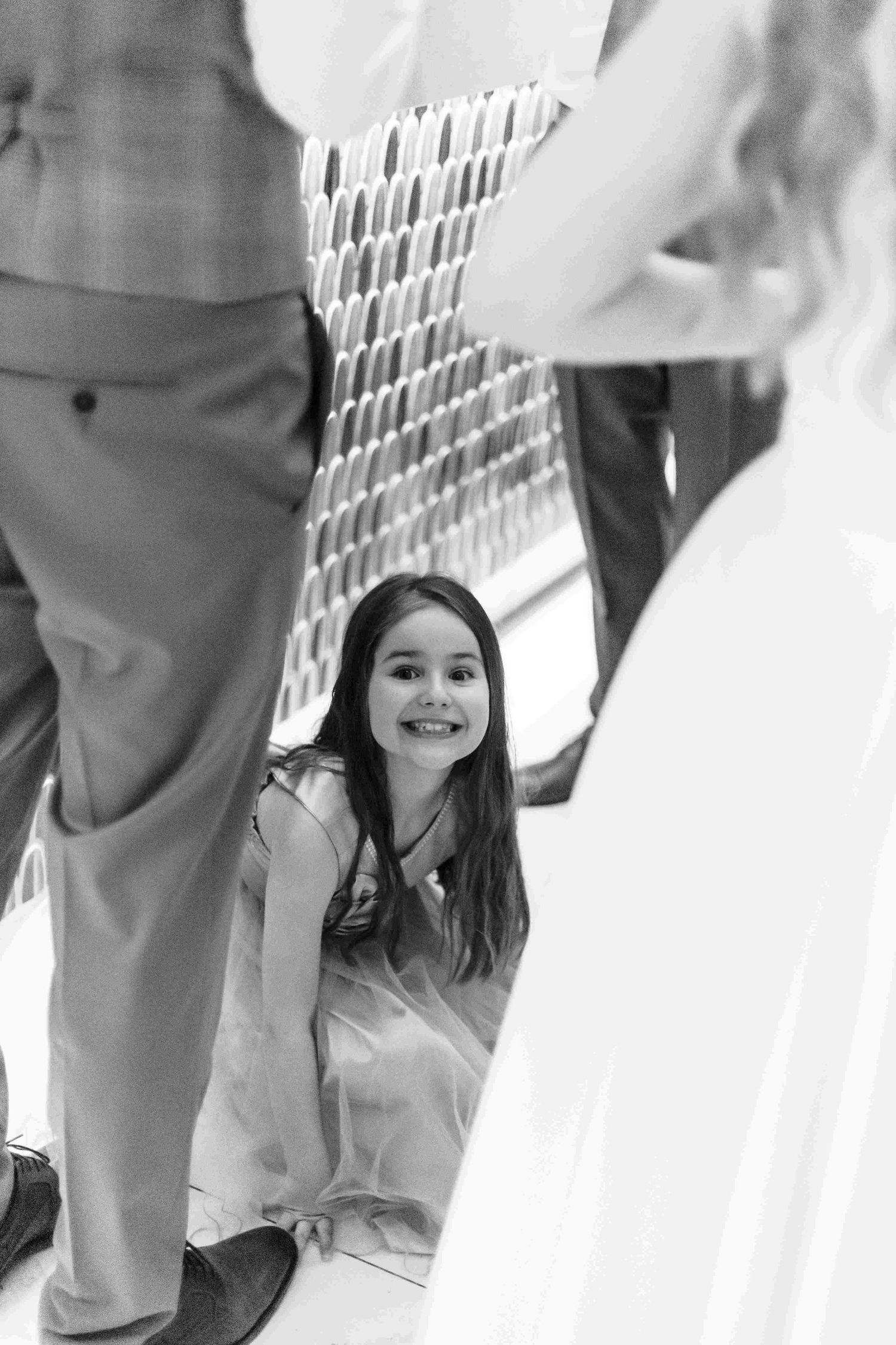 A young child peeks through white vertical slats with a joyful expression while playing.