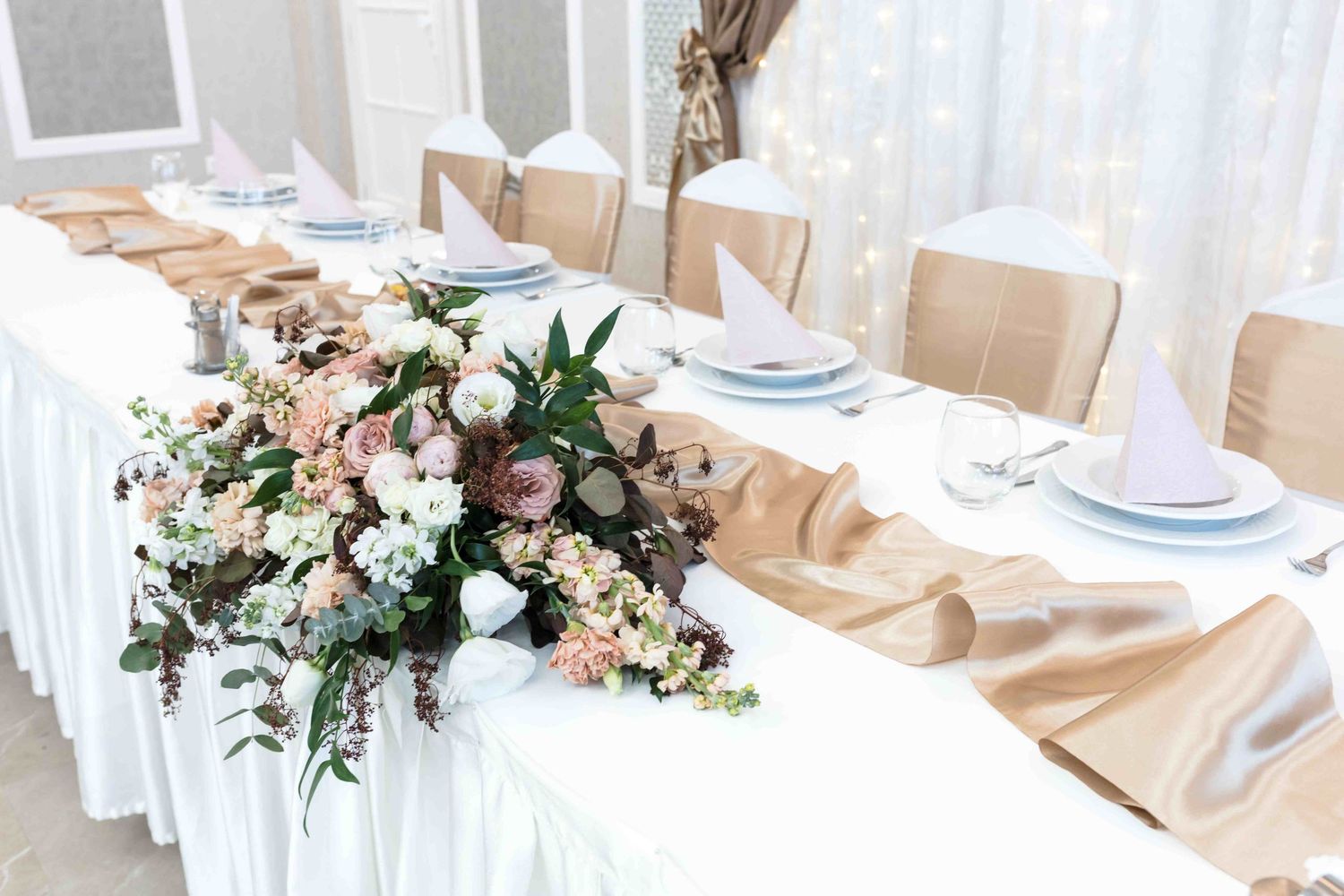 Elegant wedding table setting with blush pink and white floral centerpieces and gold accents.