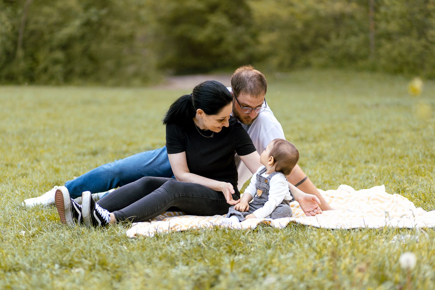 Family relaxing together on a white blanket in a green field.