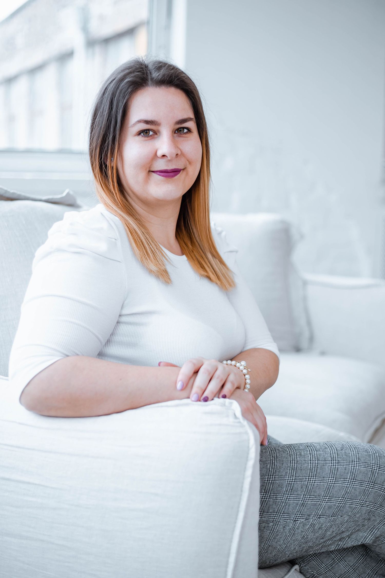 Woman relaxes on white couch wearing casual outfit in bright modern space.