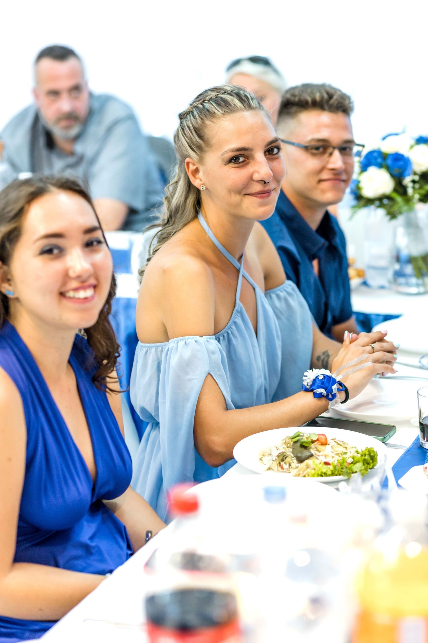 Wedding guests in blue attire enjoying a meal at a reception table decorated with blue and white flowers.
