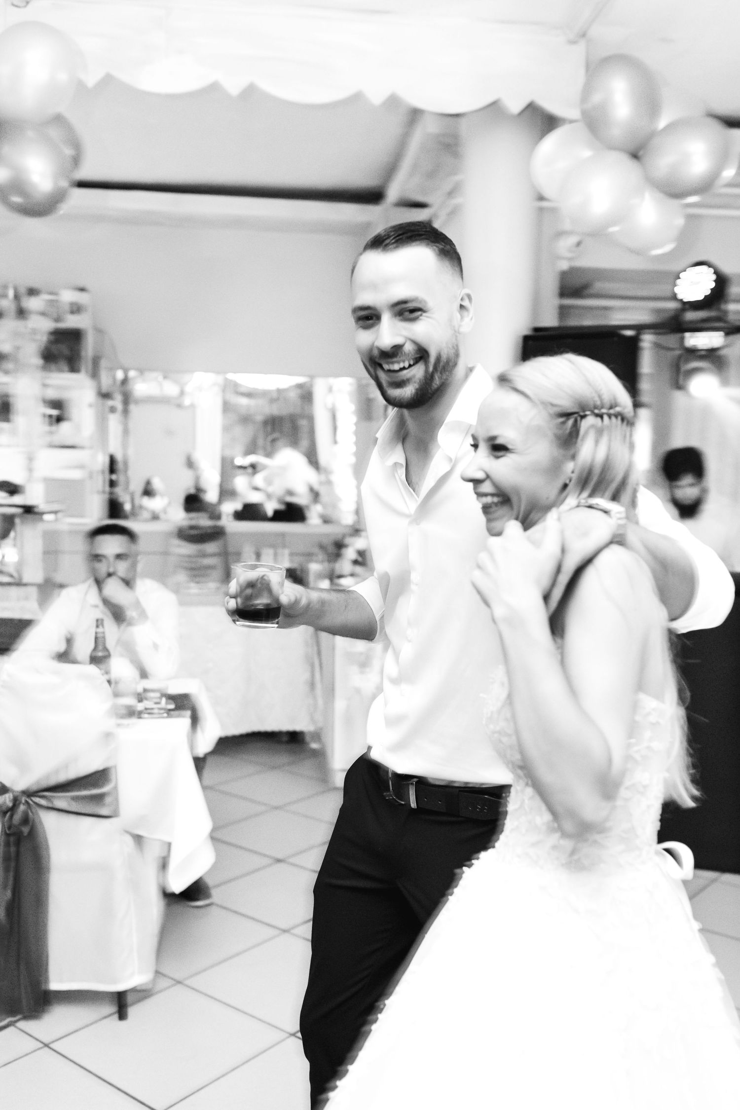 A couple shares a joyful dance moment at their wedding reception with white balloons decorating the venue.