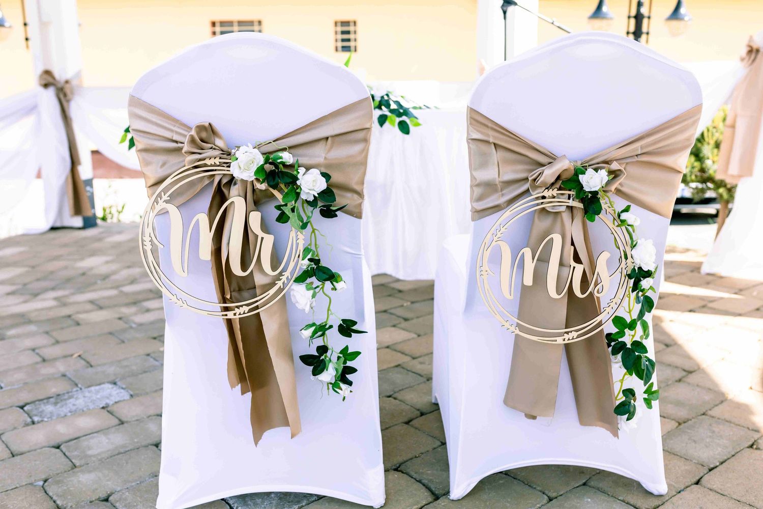 White wedding chairs decorated with burlap bows, wooden Mr and Mrs signs, and cascading green ivy at an outdoor venue.