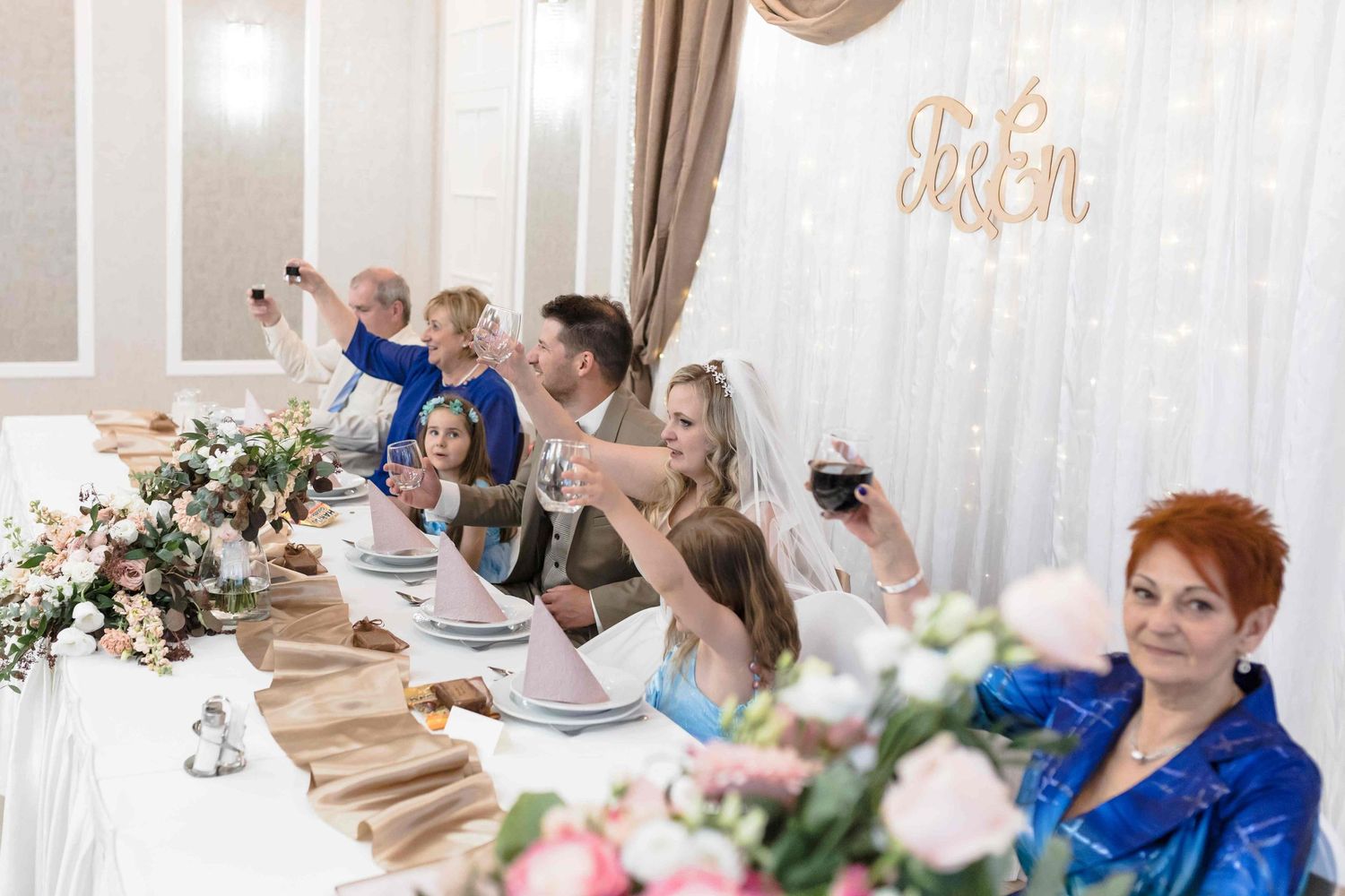 Wedding guests seated at elegant long tables decorated with floral centerpieces and white linens at a reception venue.