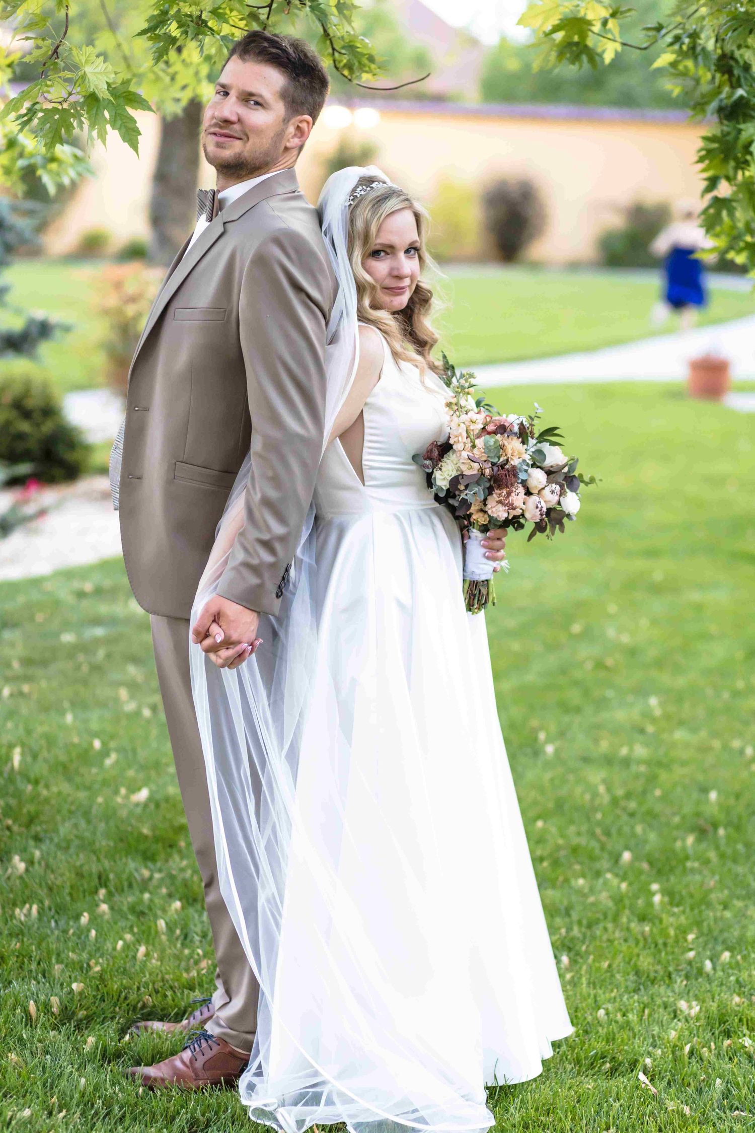 Newlyweds share a romantic moment together on a grassy lawn with green trees in the background.