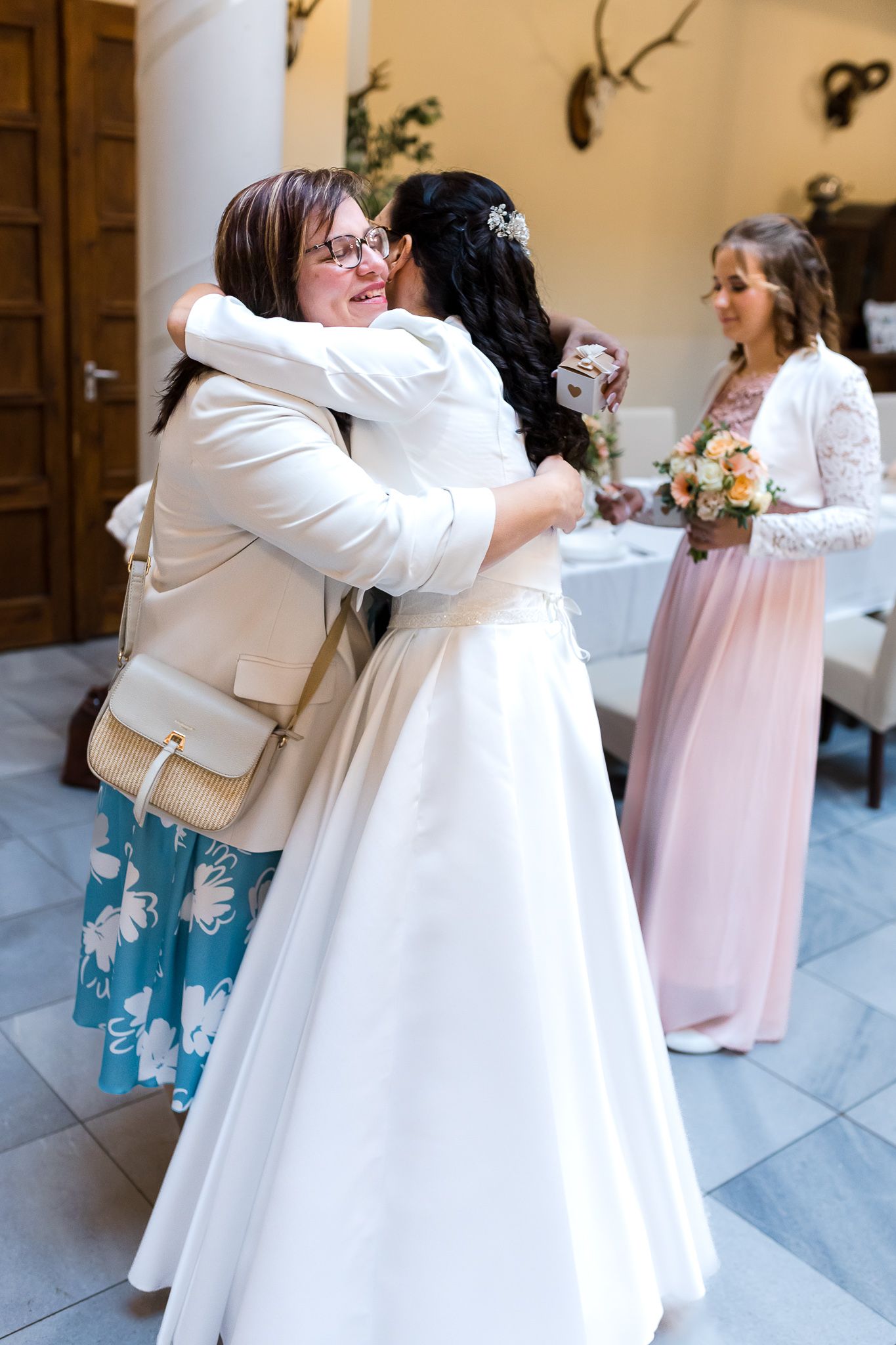 Two people share an emotional embrace in white formal attire during a special celebration moment.
