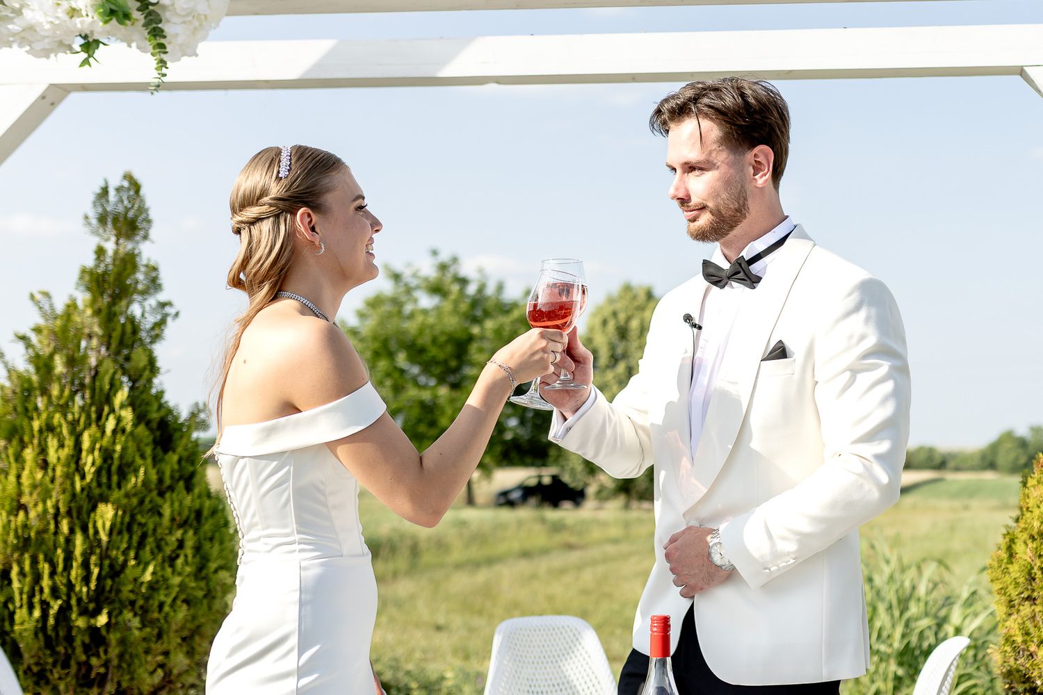 Wedding couple toasts with wine glasses during outdoor celebration.