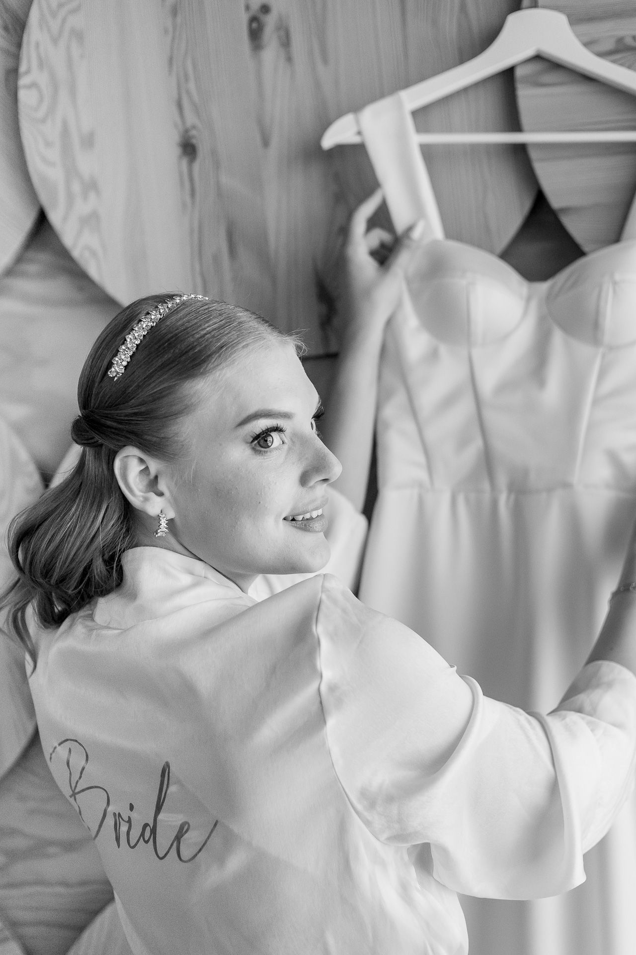 A person wearing a white robe with 'Bride' text adjusts a wedding dress on display.