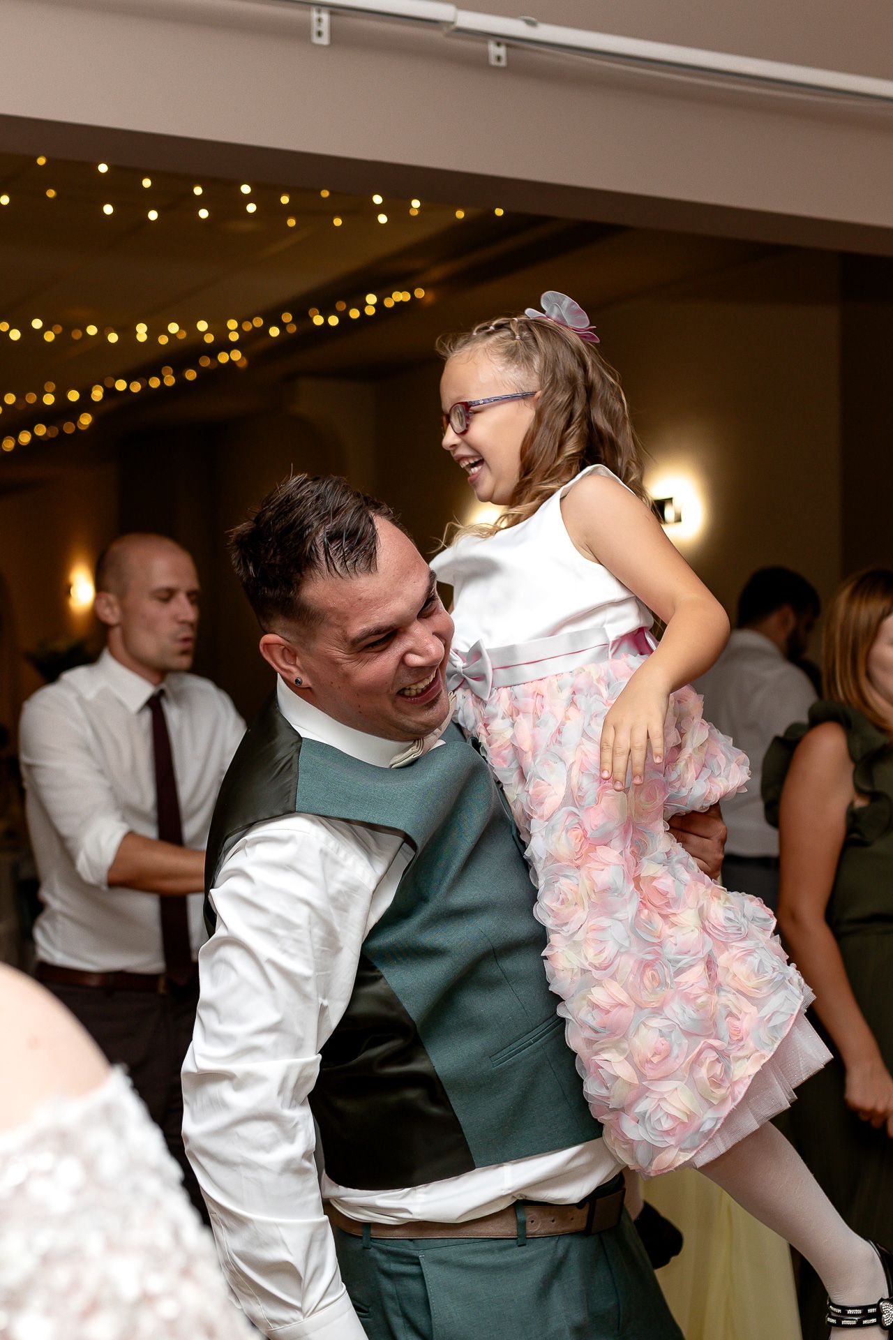 A couple dances together at a wedding reception under string lights, with the man dipping his dance partner.