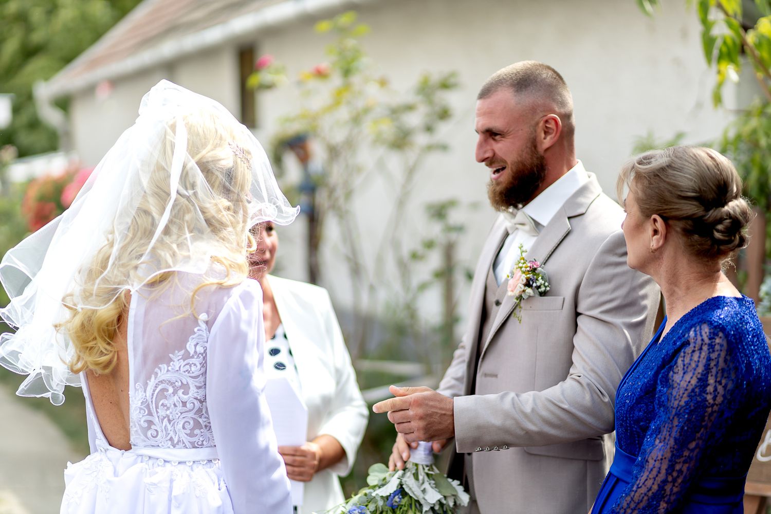Wedding celebration outdoors with guests in gray and blue attire enjoying a festive moment.