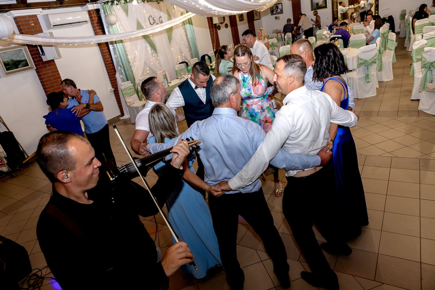 A group of people dancing and celebrating at an indoor event with decorative banners and streamers.