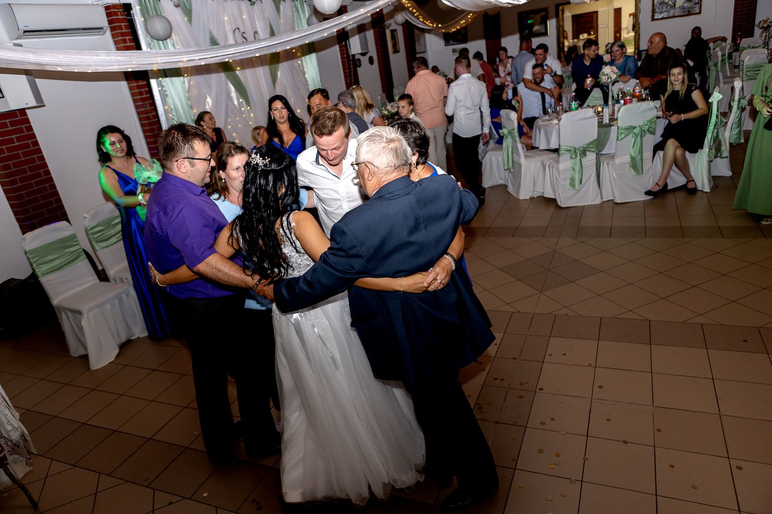 Couples dancing together at an elegant wedding reception in a banquet hall with white decorations.