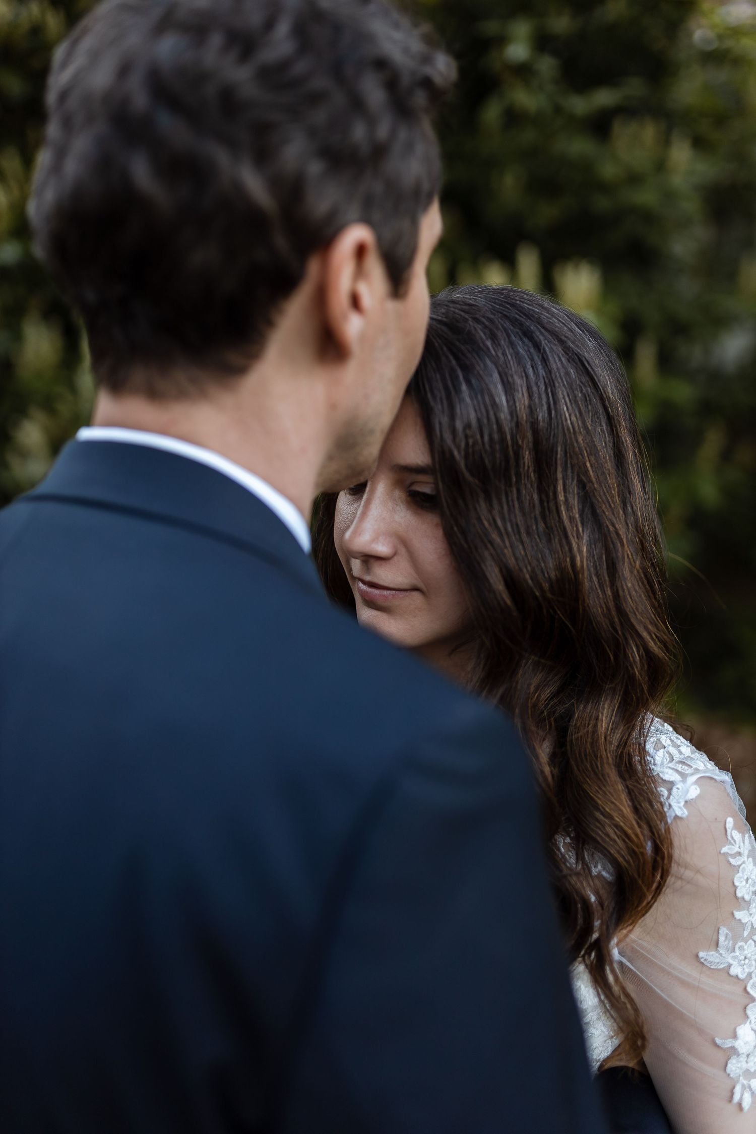 A romantic wedding moment captured between a couple in formal attire against a blurred natural background.