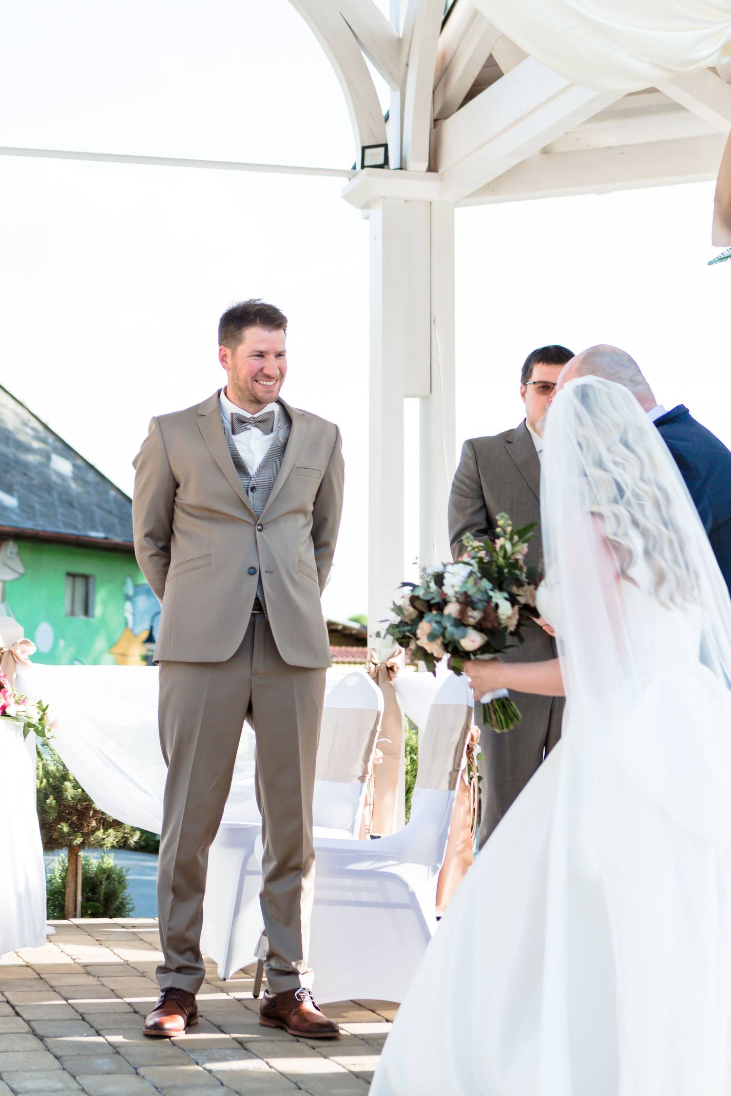 A bride and groom share a joyful moment during their first look on a white porch at their wedding.