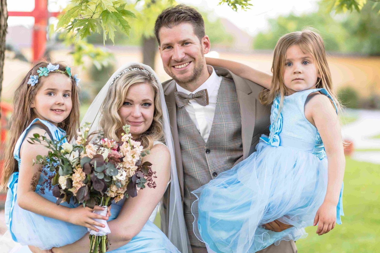 A group of wedding party members in light blue dresses and gray suits pose together outdoors.