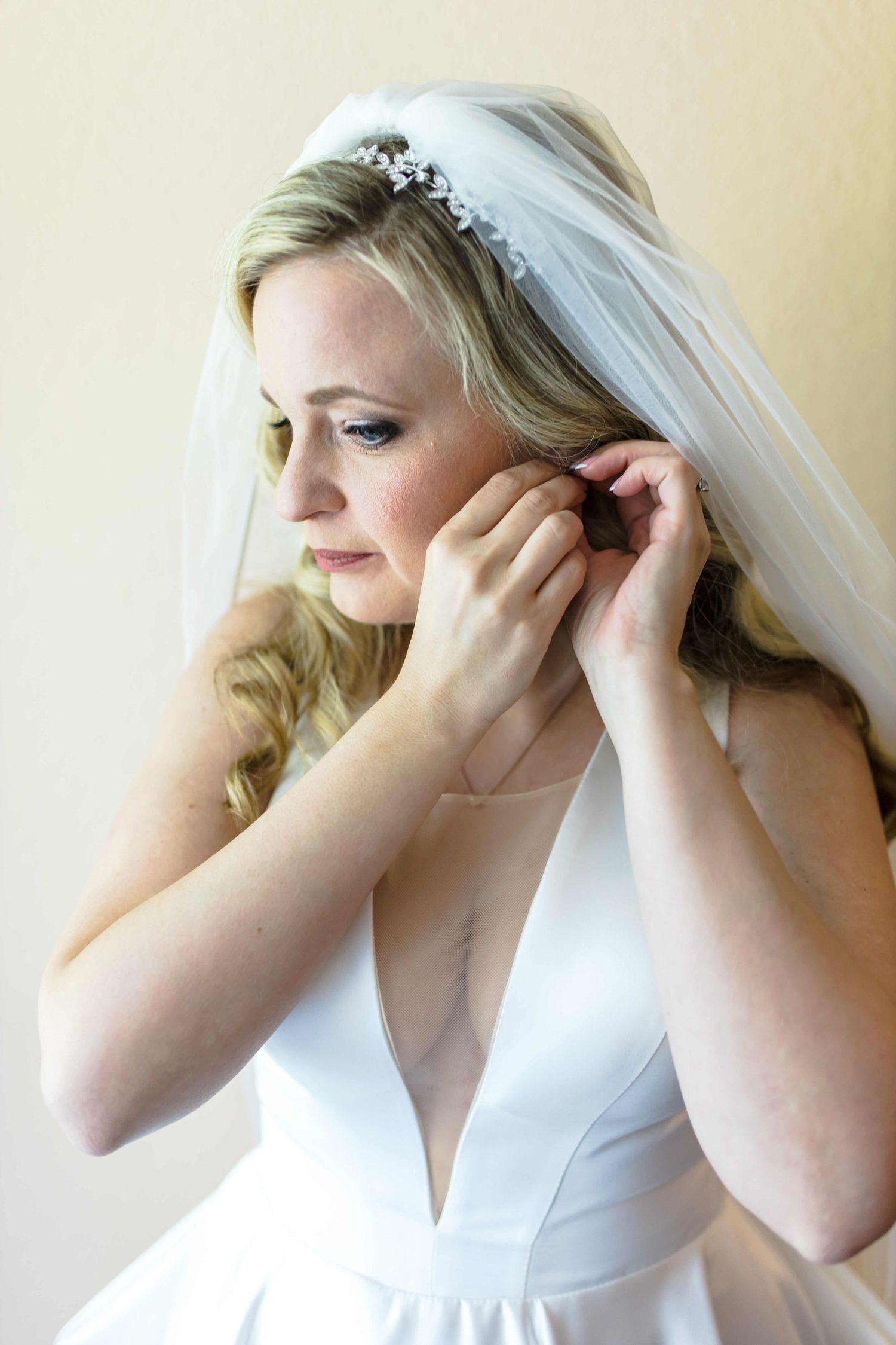 A bride in a white dress adjusts her veil while getting ready for her wedding ceremony.