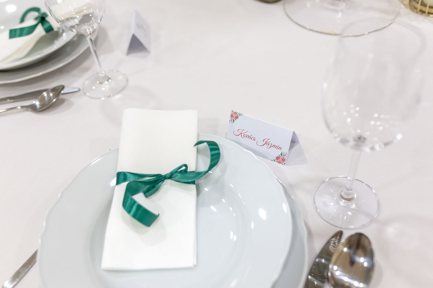 Elegant white and teal wedding reception table setting with place cards and glassware.