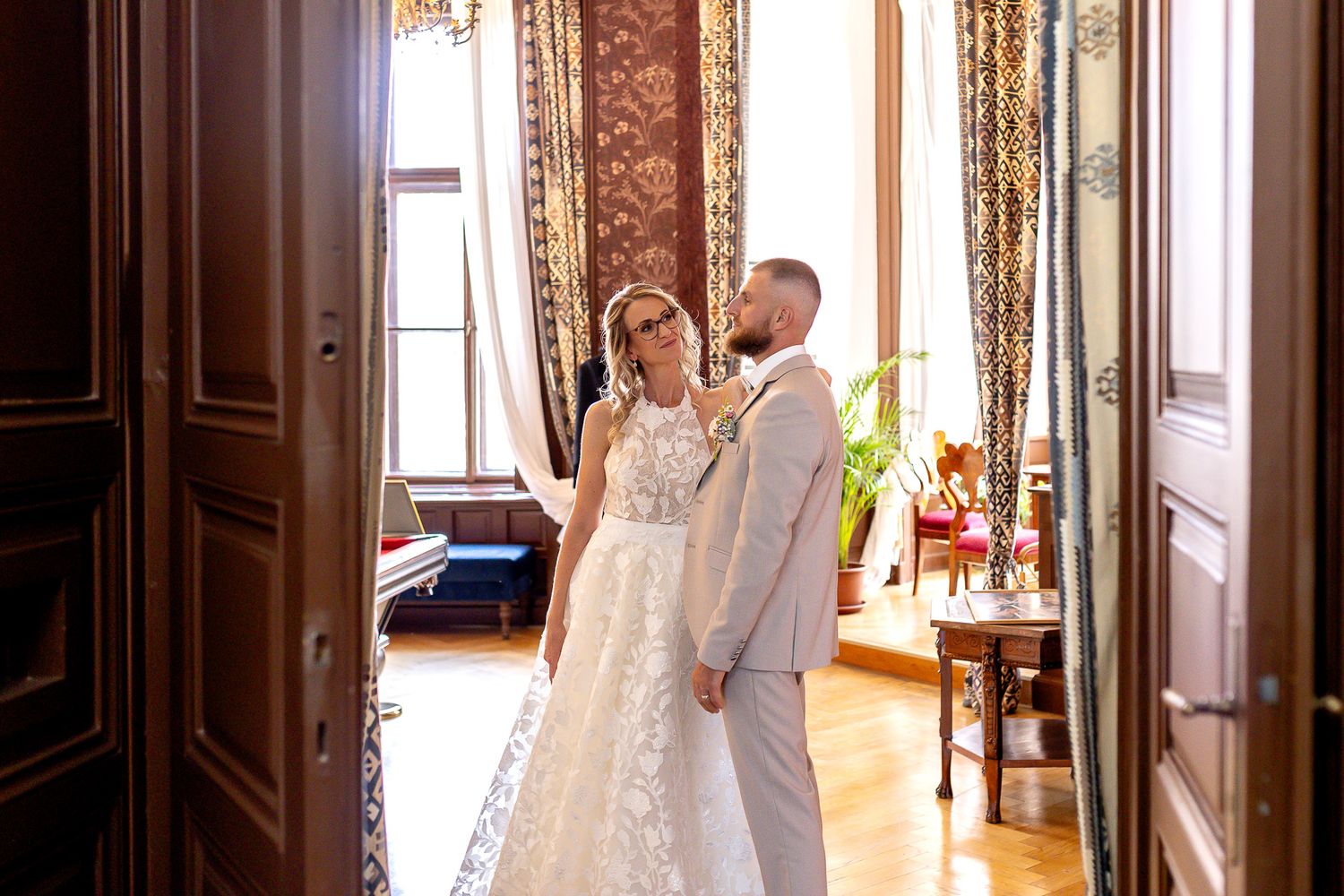 A couple embraces during their first look in a sunlit hallway with classic architectural details.