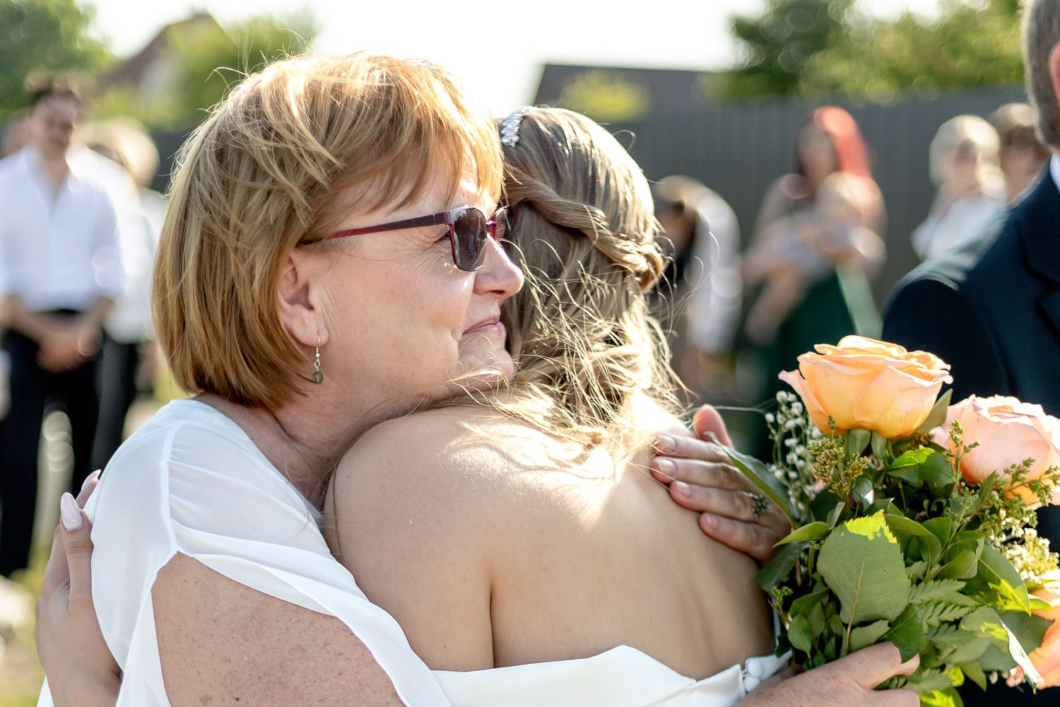 Wedding party embraces during emotional outdoor celebration with greenery.