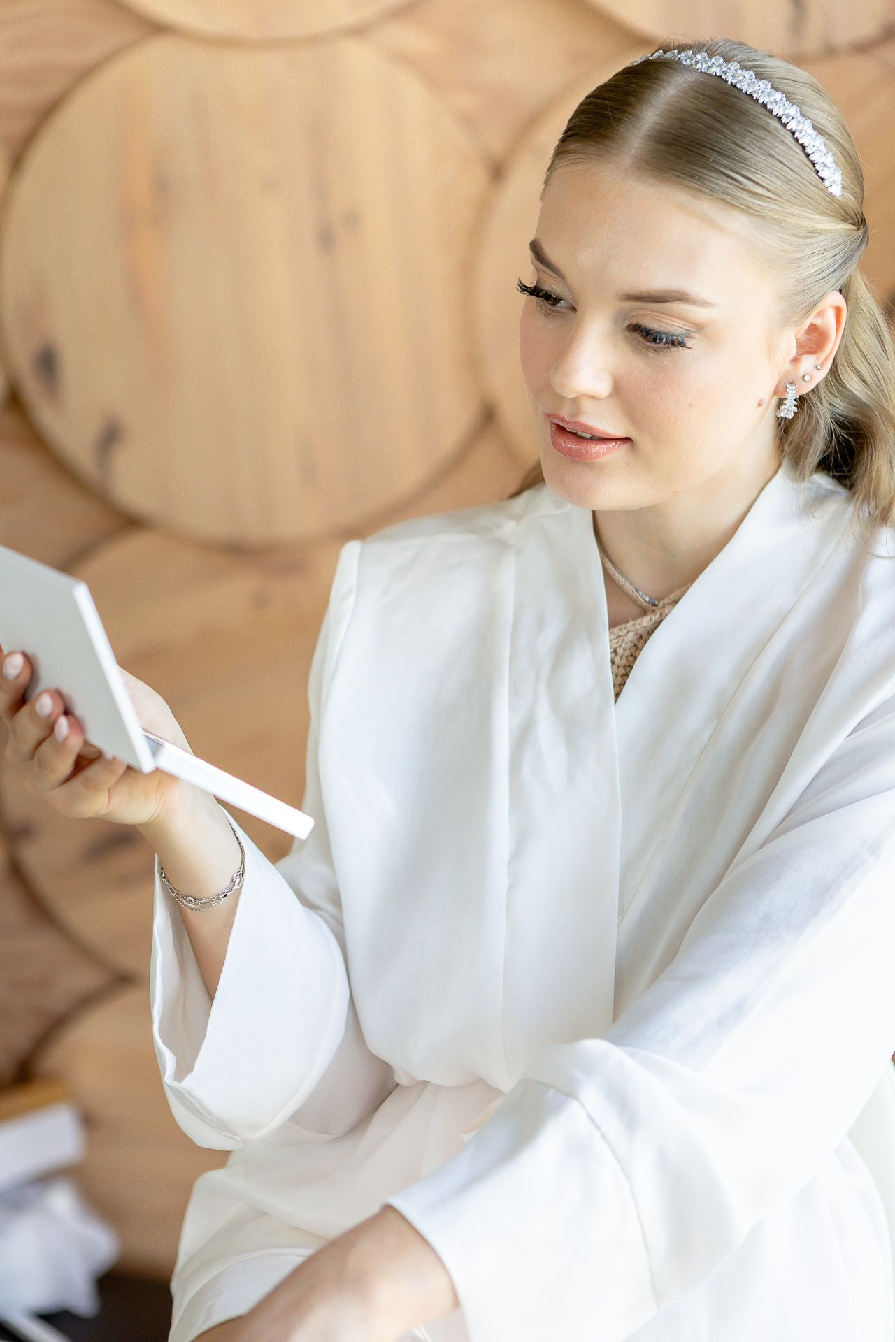 Person in white robe and sparkly headpiece posing against wooden wall.
