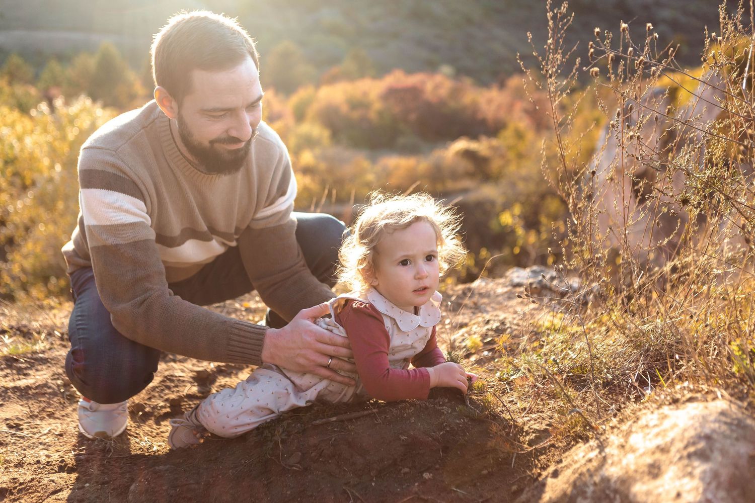 Family enjoying a playful moment together on a grassy hillside during golden hour sunset.