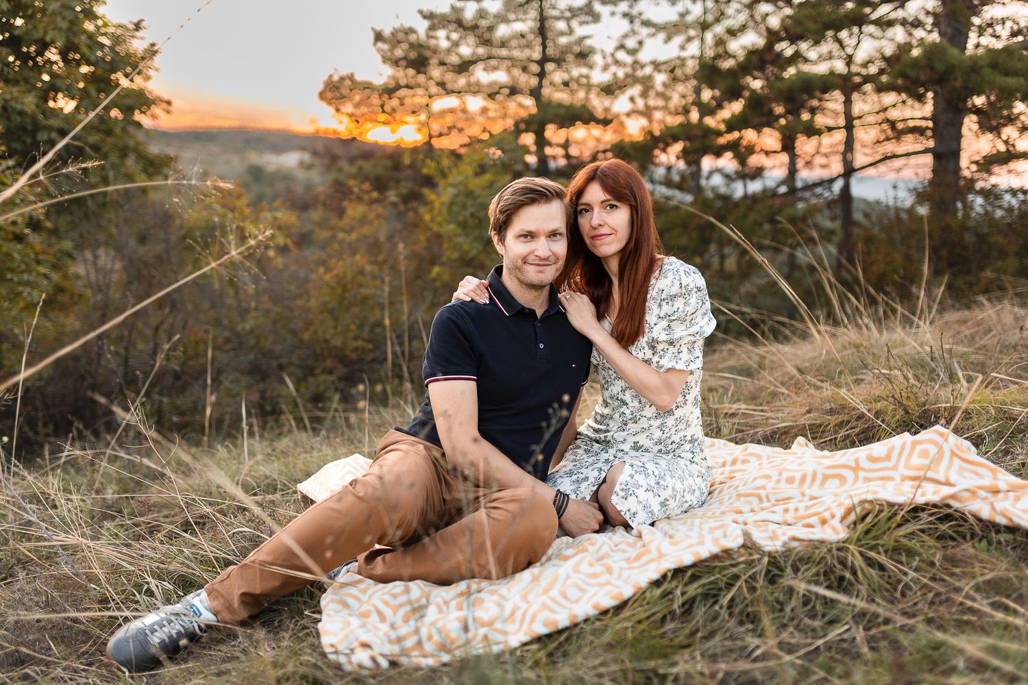 Couple shares intimate moment while sitting together on hillside during golden hour.