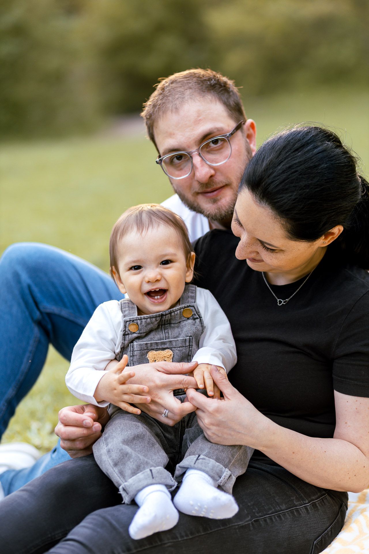 Baby laughing during outdoor family photo session in casual attire.