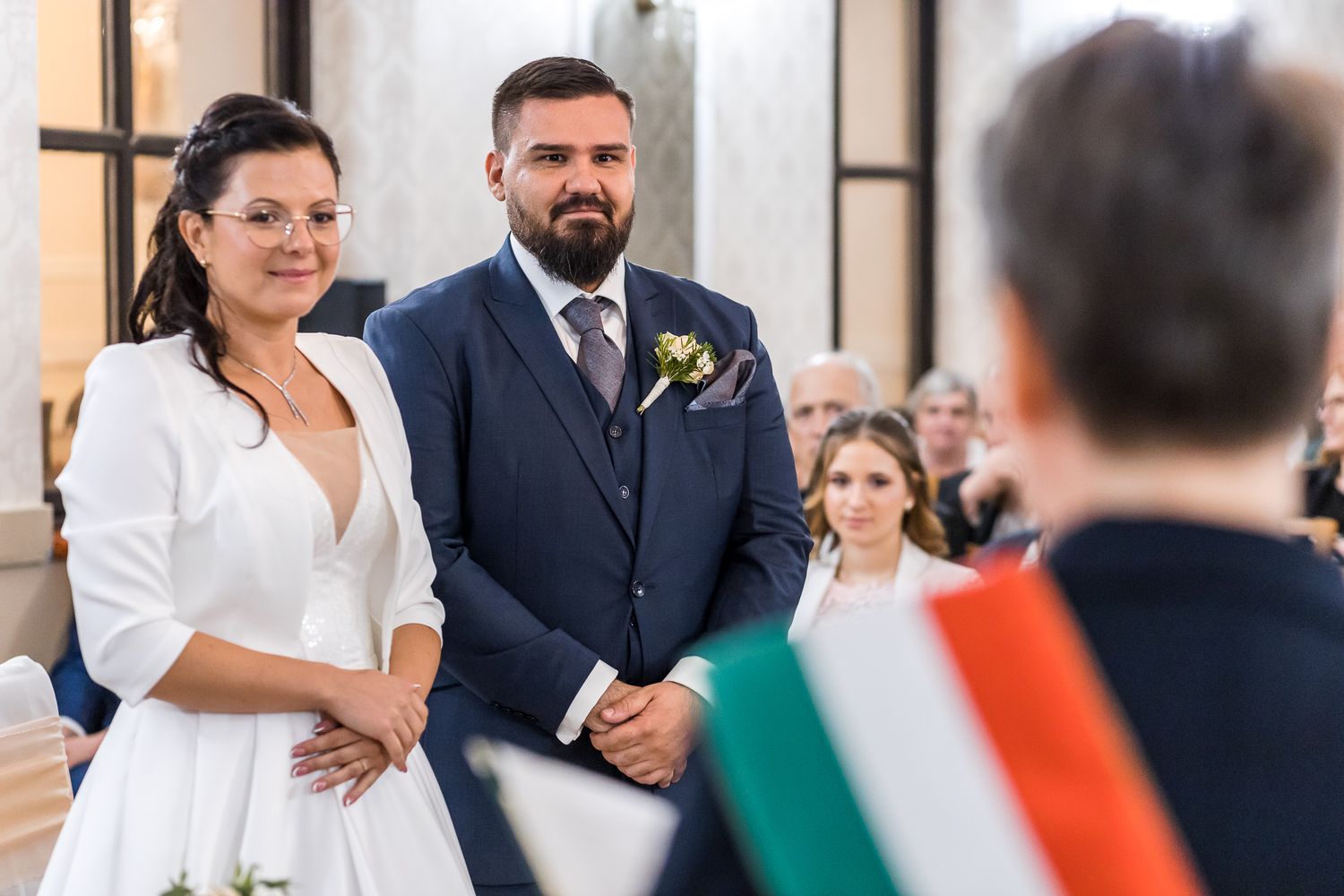 A wedding couple walks down a church aisle while guests wave Irish flags in celebration.