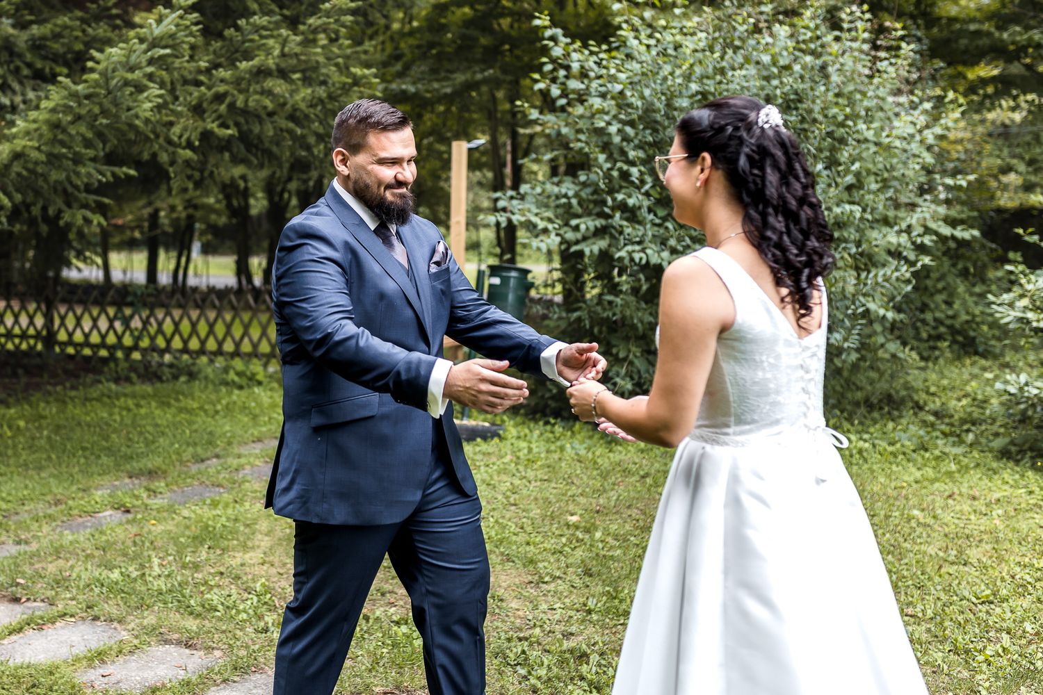 A couple in formal wedding attire sharing a joyful moment together in a garden setting.