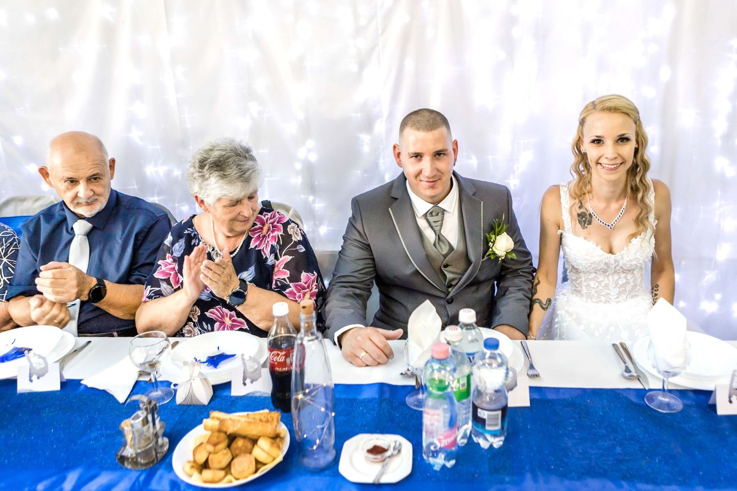 Wedding guests seated at tables enjoy a reception meal with drinks and decor in a bright indoor venue.