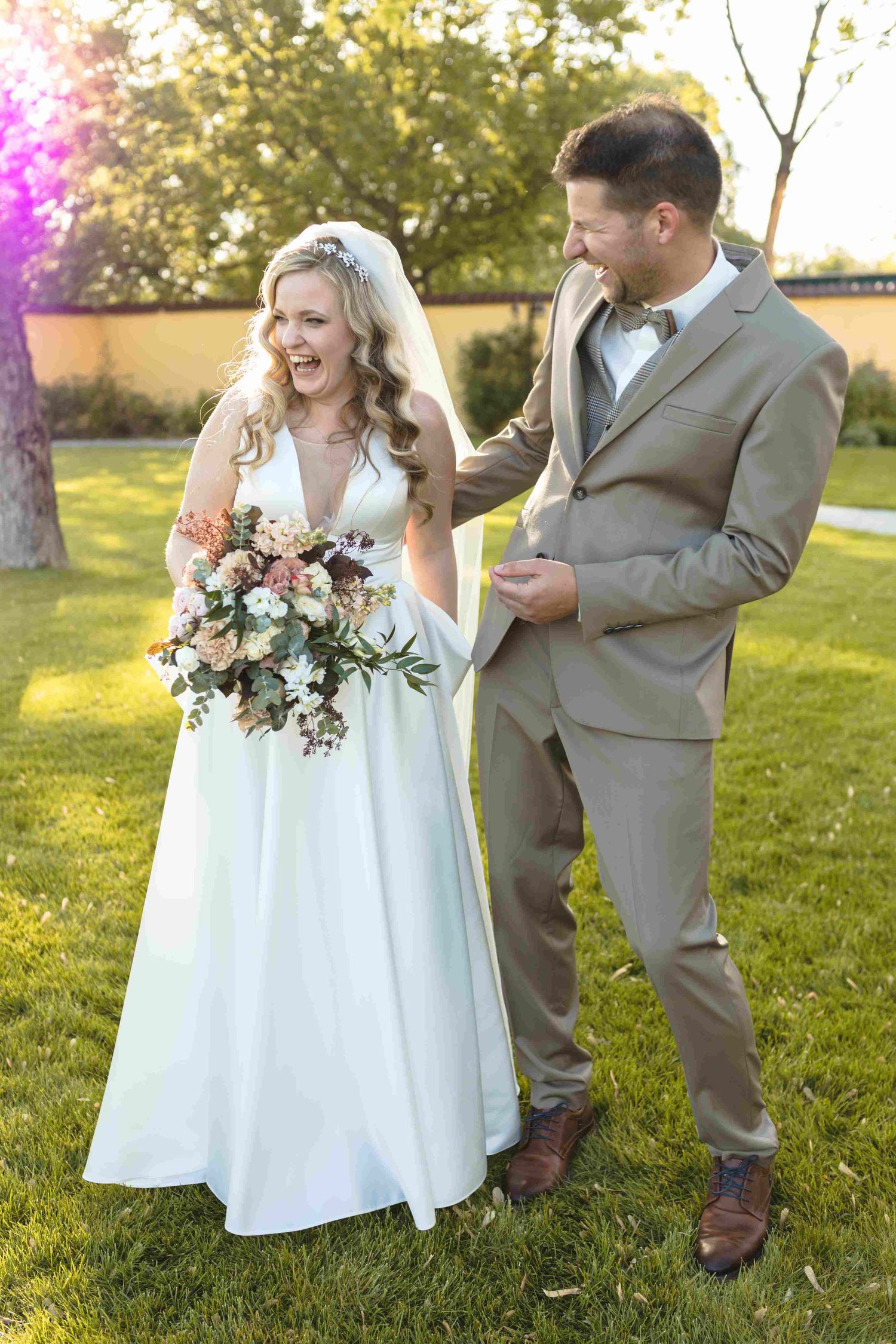 A couple shares a joyful moment together on their wedding day in a sunlit garden setting.