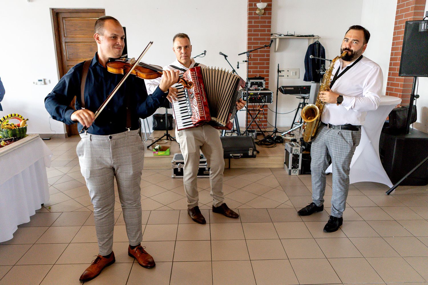Musicians in white shirts perform with violins and other string instruments on an outdoor porch or patio.