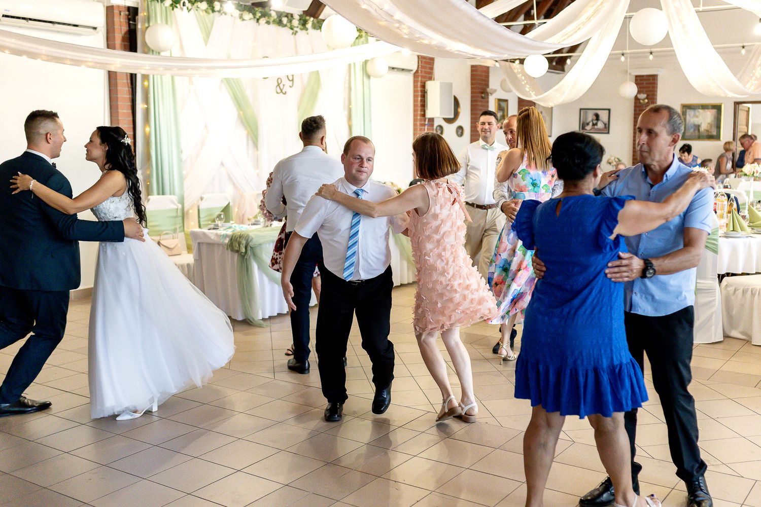 People dancing in a line at a wedding reception with streamers and decorations visible in the background.