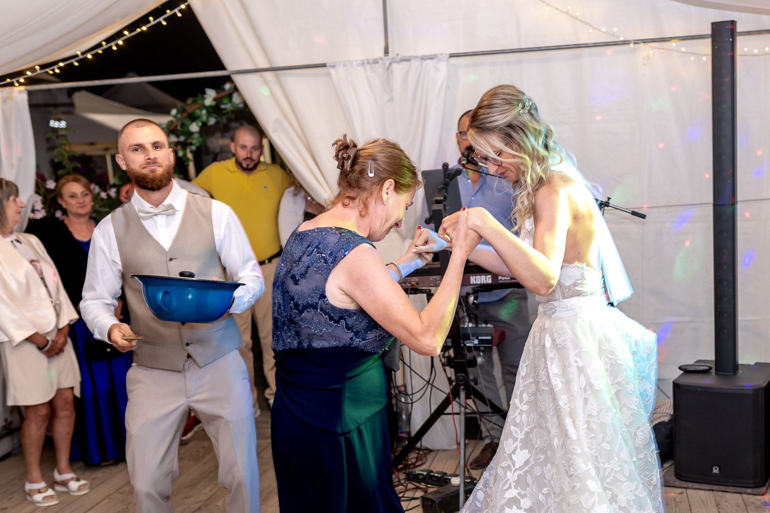 Wedding guests dance together in a white tent during an evening reception celebration.