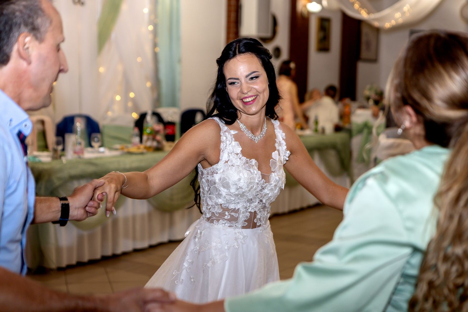 Wedding guests dance and celebrate on the dance floor at an indoor reception with twinkle lights and decorations.