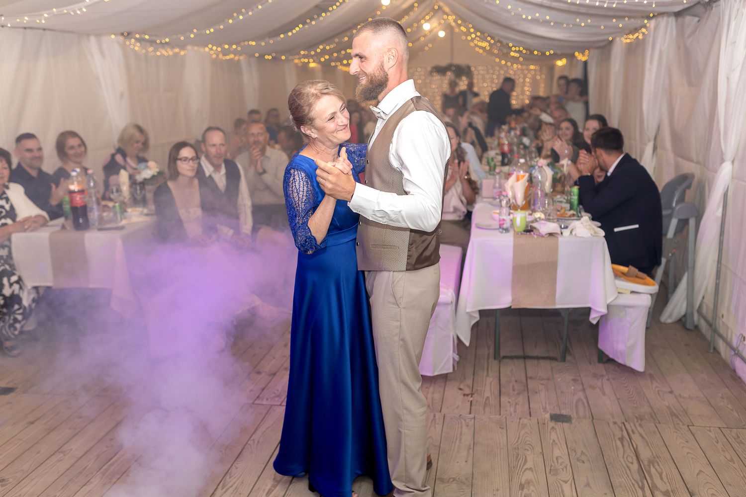 Wedding reception dance floor scene with guests in formal attire enjoying a celebration in a white draped venue.