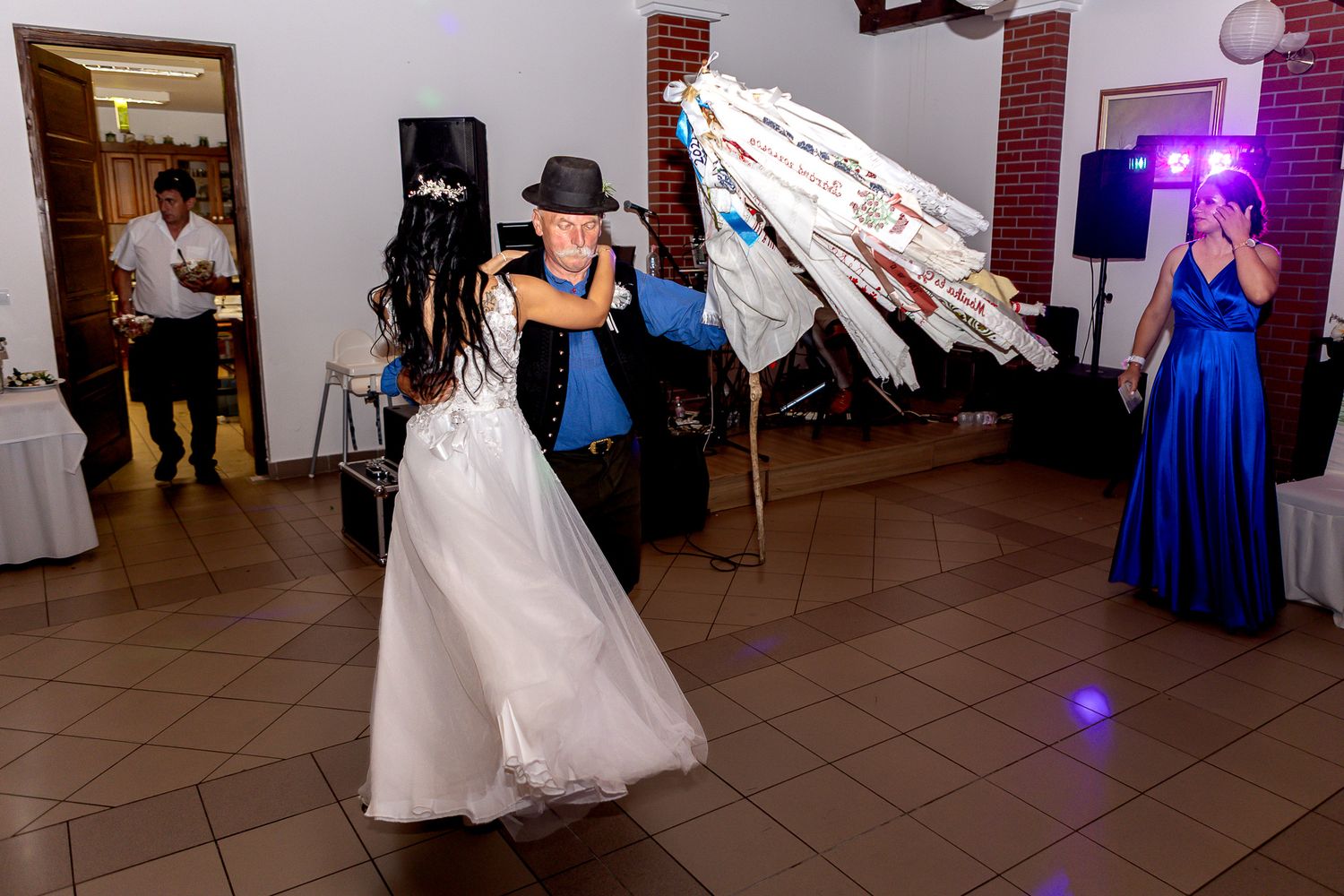 Wedding guests dance together on a tiled dance floor during an evening reception celebration.