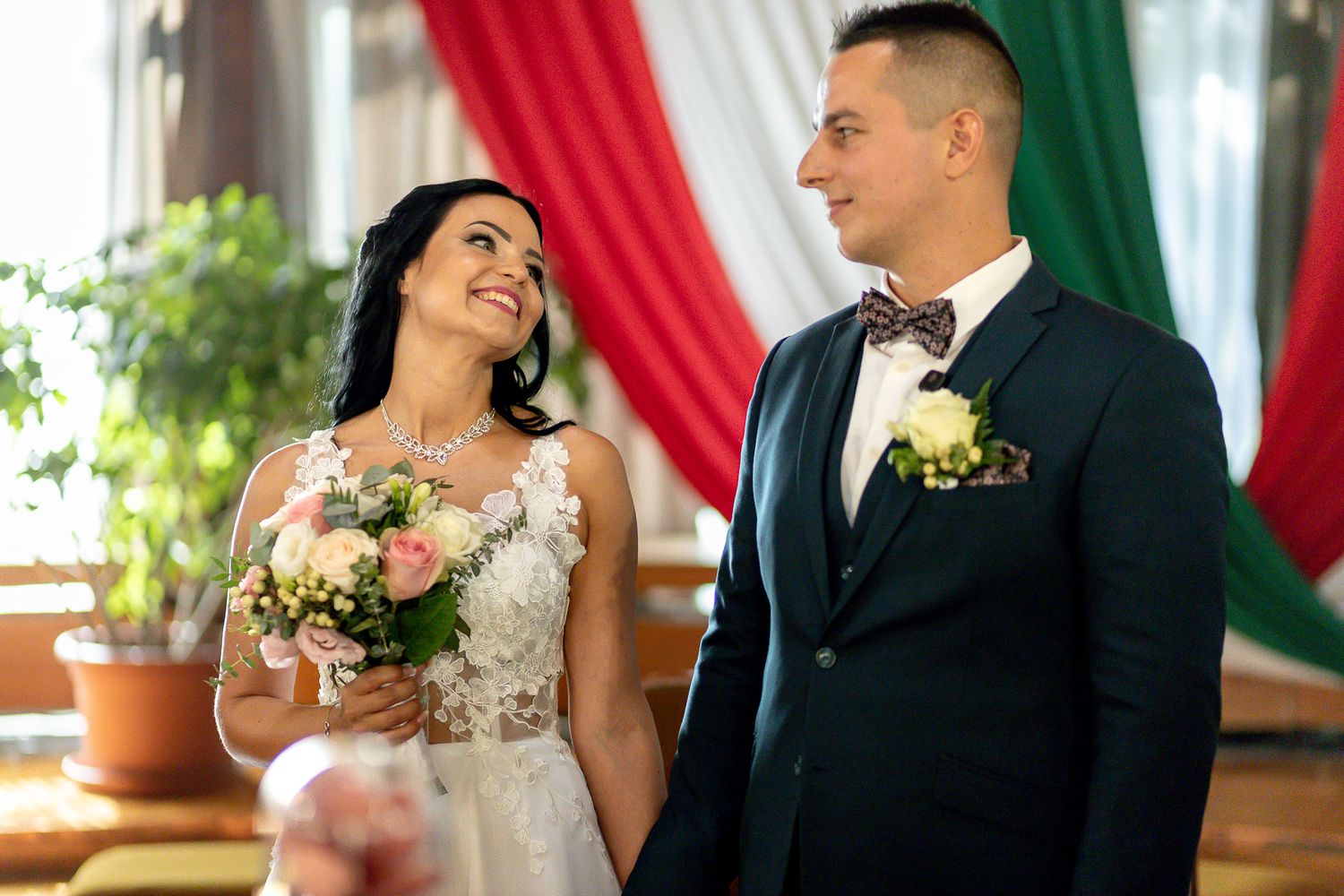 Wedding couple shares intimate moments during their ceremony with red and green drapery in the background.