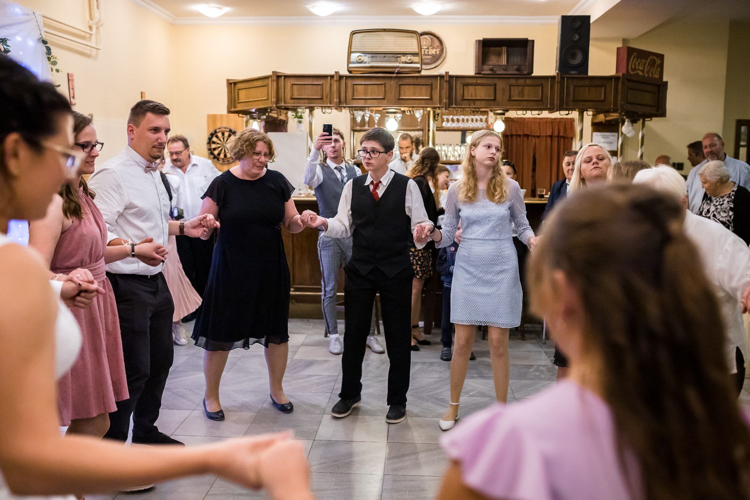 Wedding guests dance and celebrate together on a crowded dance floor at an indoor reception venue.