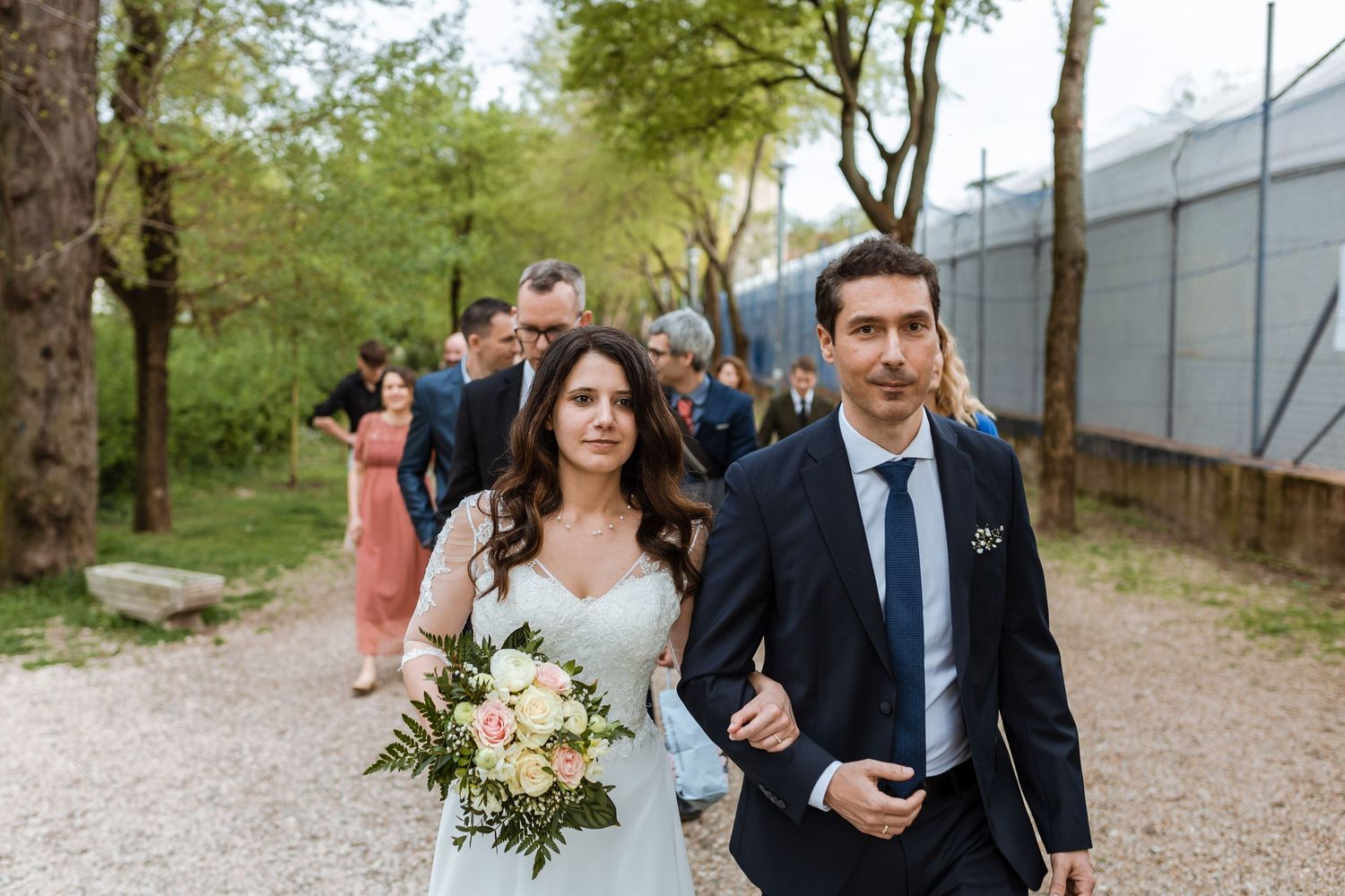 Guests walk along a gravel path at an outdoor wedding venue surrounded by greenery.