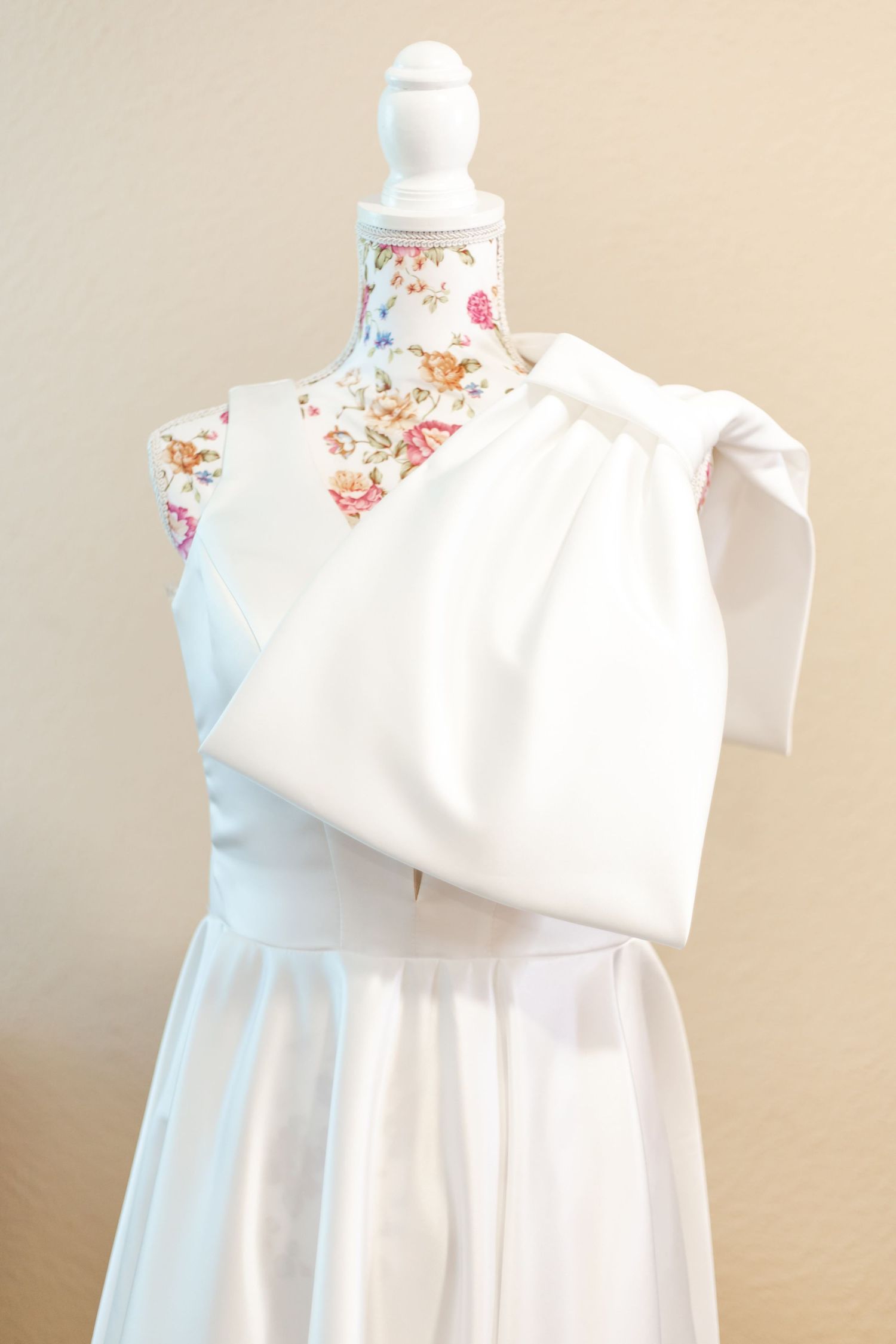 Elegant white baby dress with floral collar displayed on mannequin against neutral background.