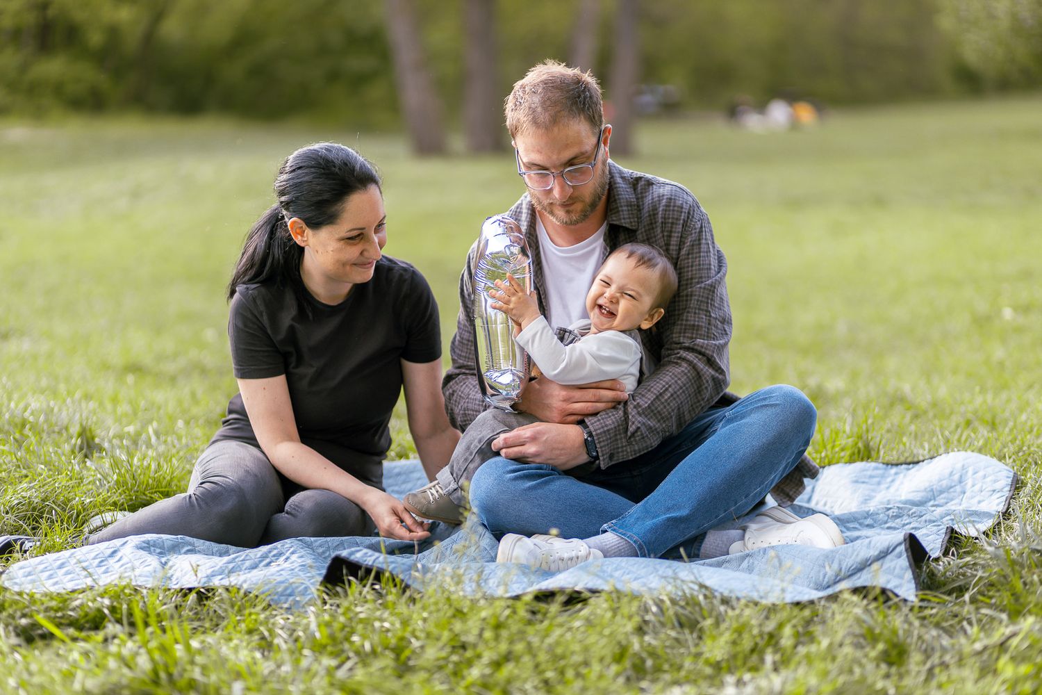 Family enjoying quality time together on blanket in sunny park setting.