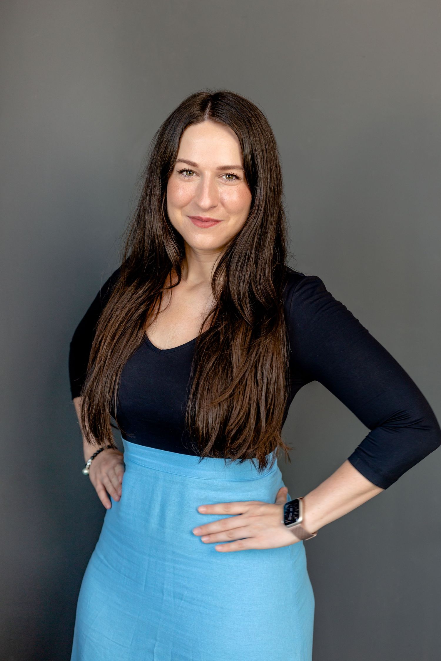 A person in a black top and light blue bottom poses confidently against a grey background.