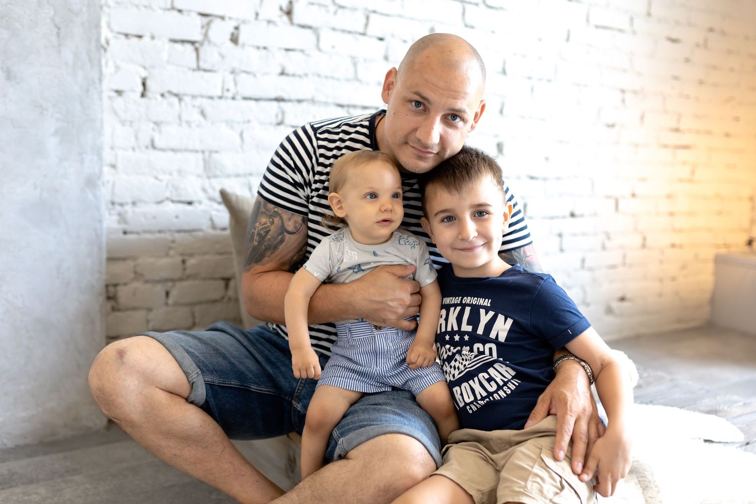 Indoor family photoshoot with white brick wall background and casual styling.