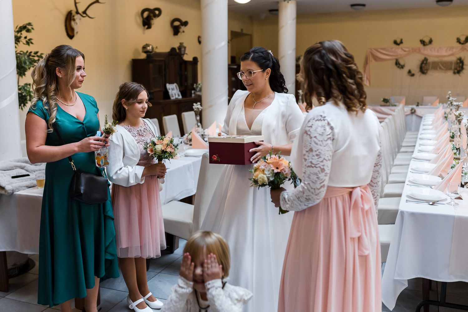 Wedding party members in pink and teal dresses gather at a reception venue for celebration.