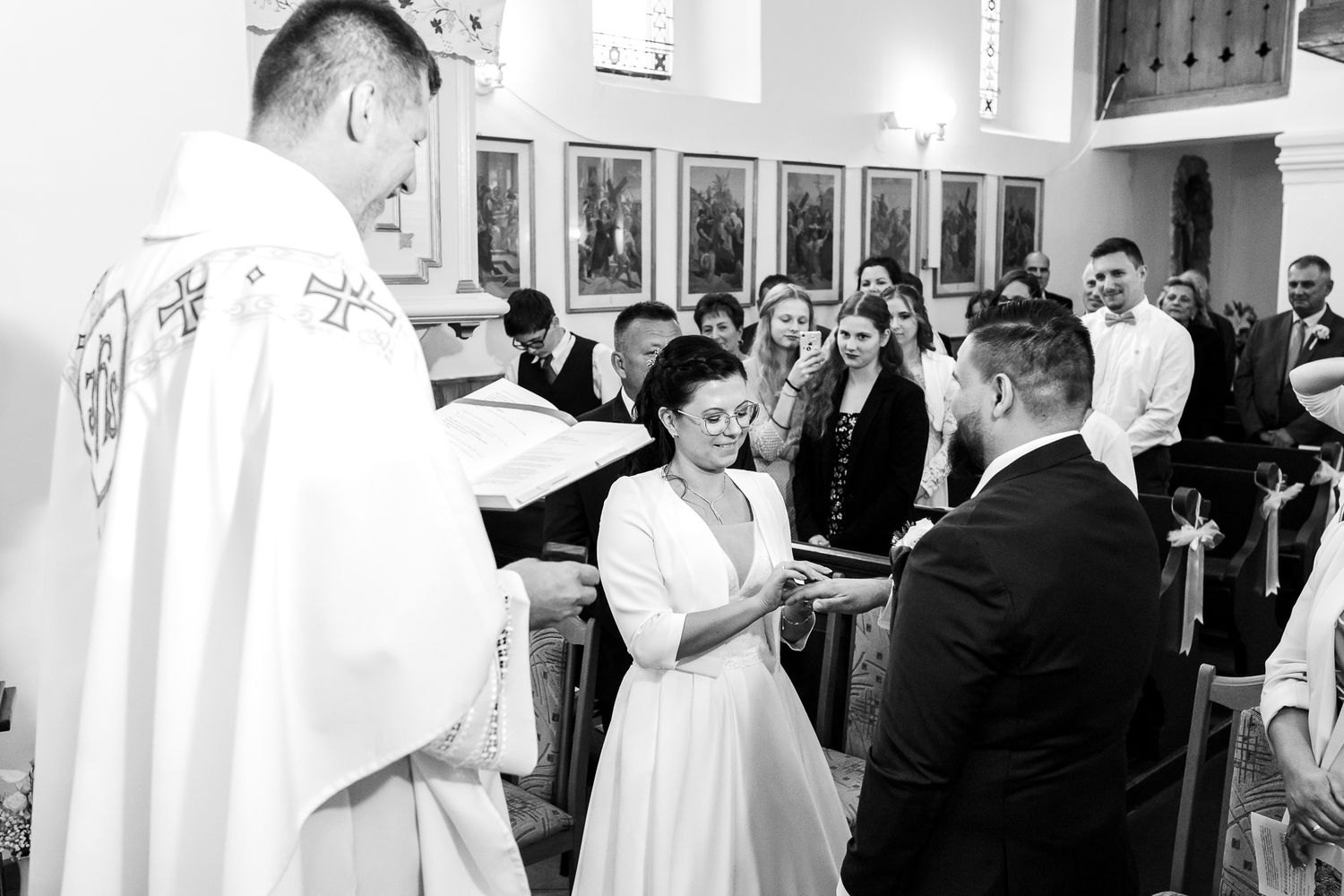 Wedding ceremony in a church with attendees in white robes and formal attire gathered around an altar.