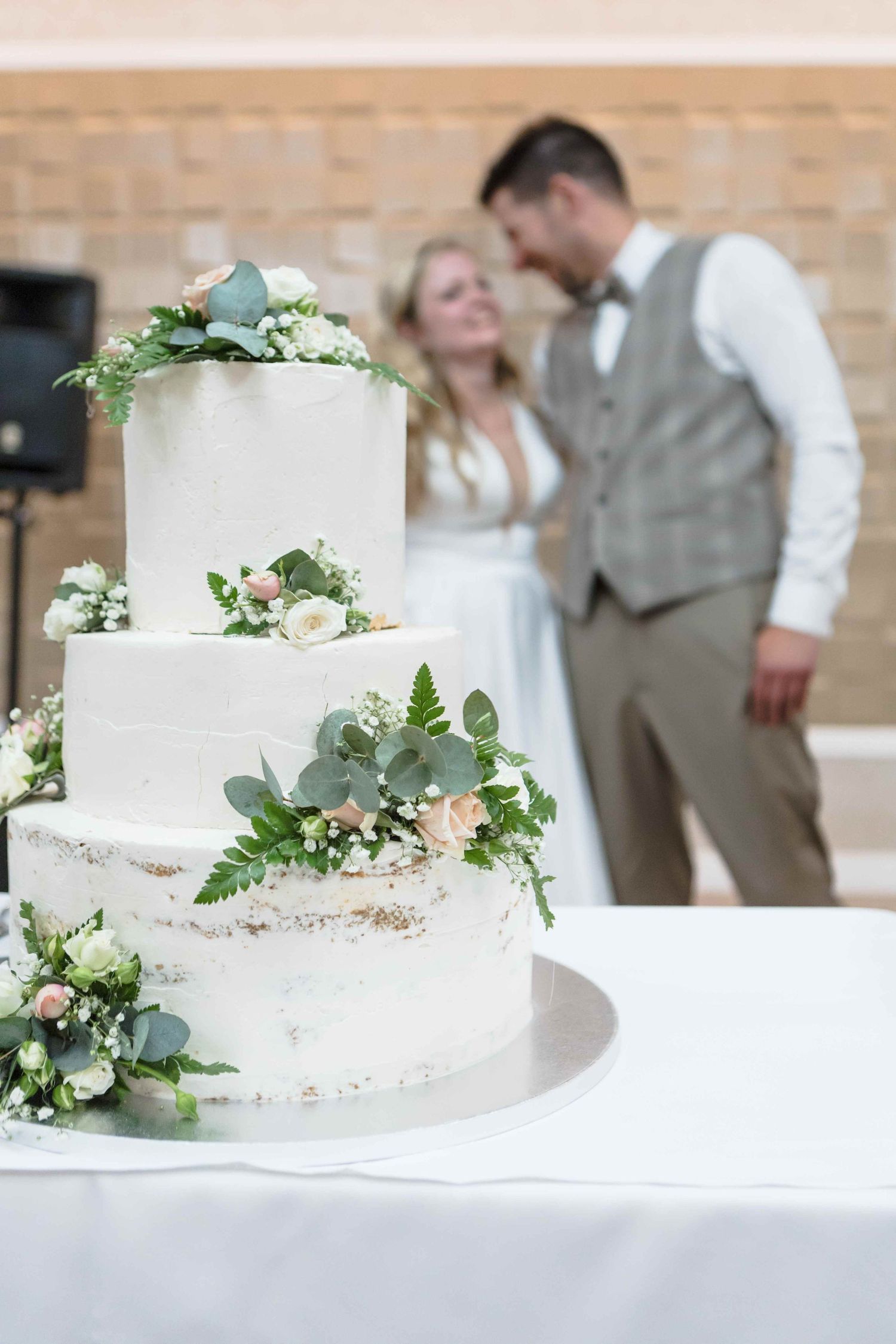 White wedding cake decorated with eucalyptus leaves and white flowers shown from multiple angles on display.