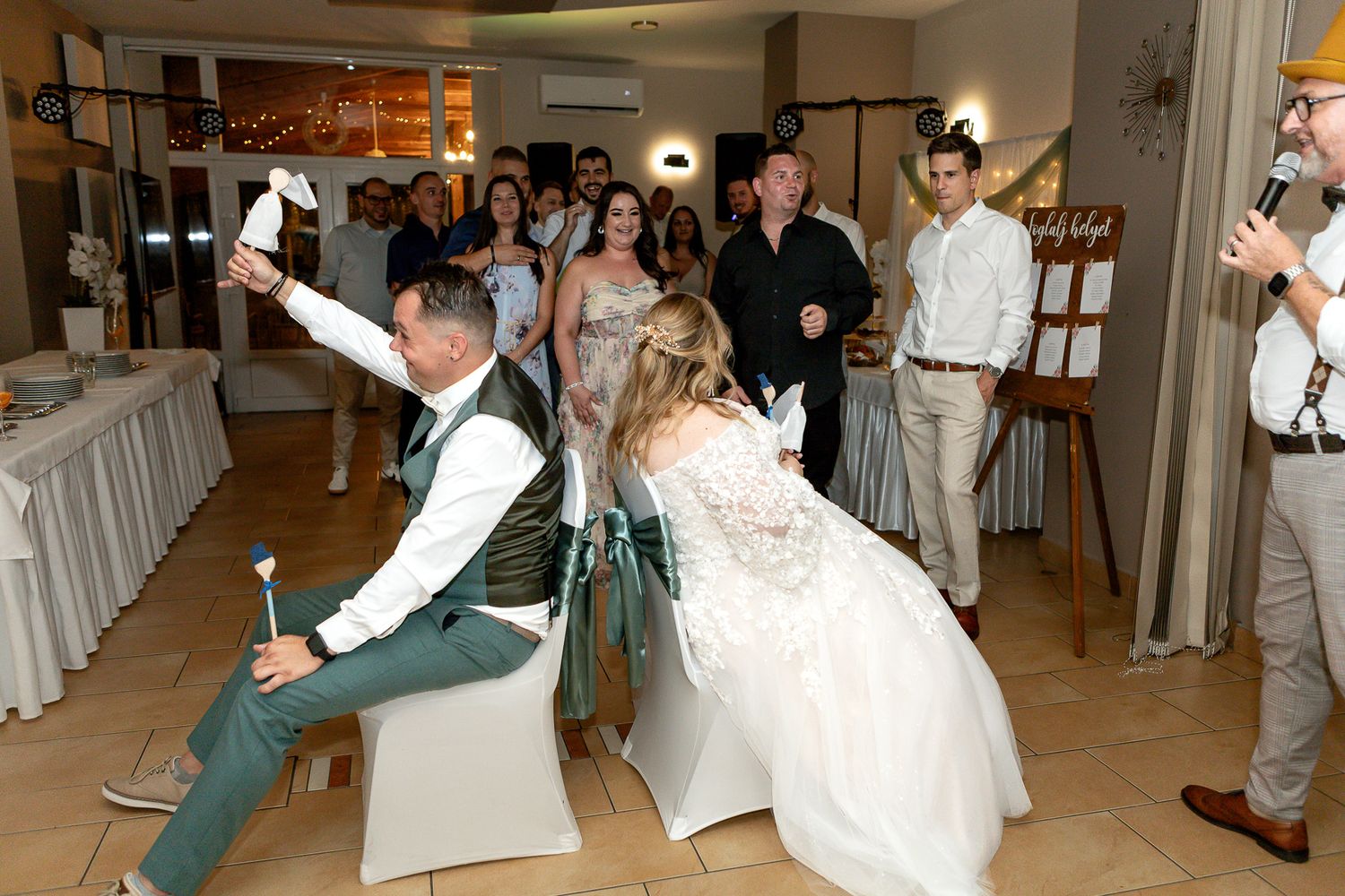 Wedding guests dance together during a reception in a brightly lit indoor venue with string lights.