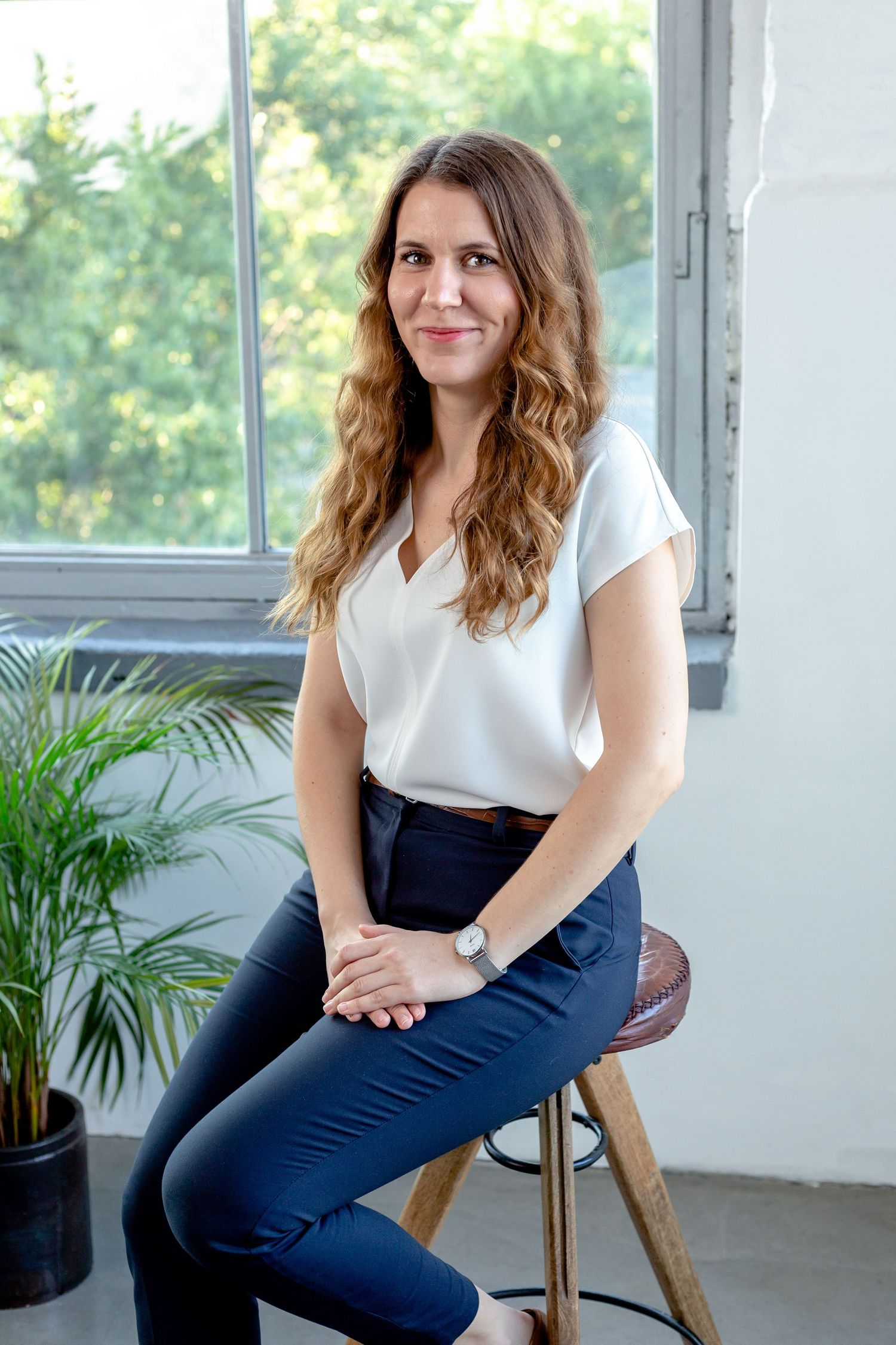 Casual business portraits by sunny window with plants visible in background.